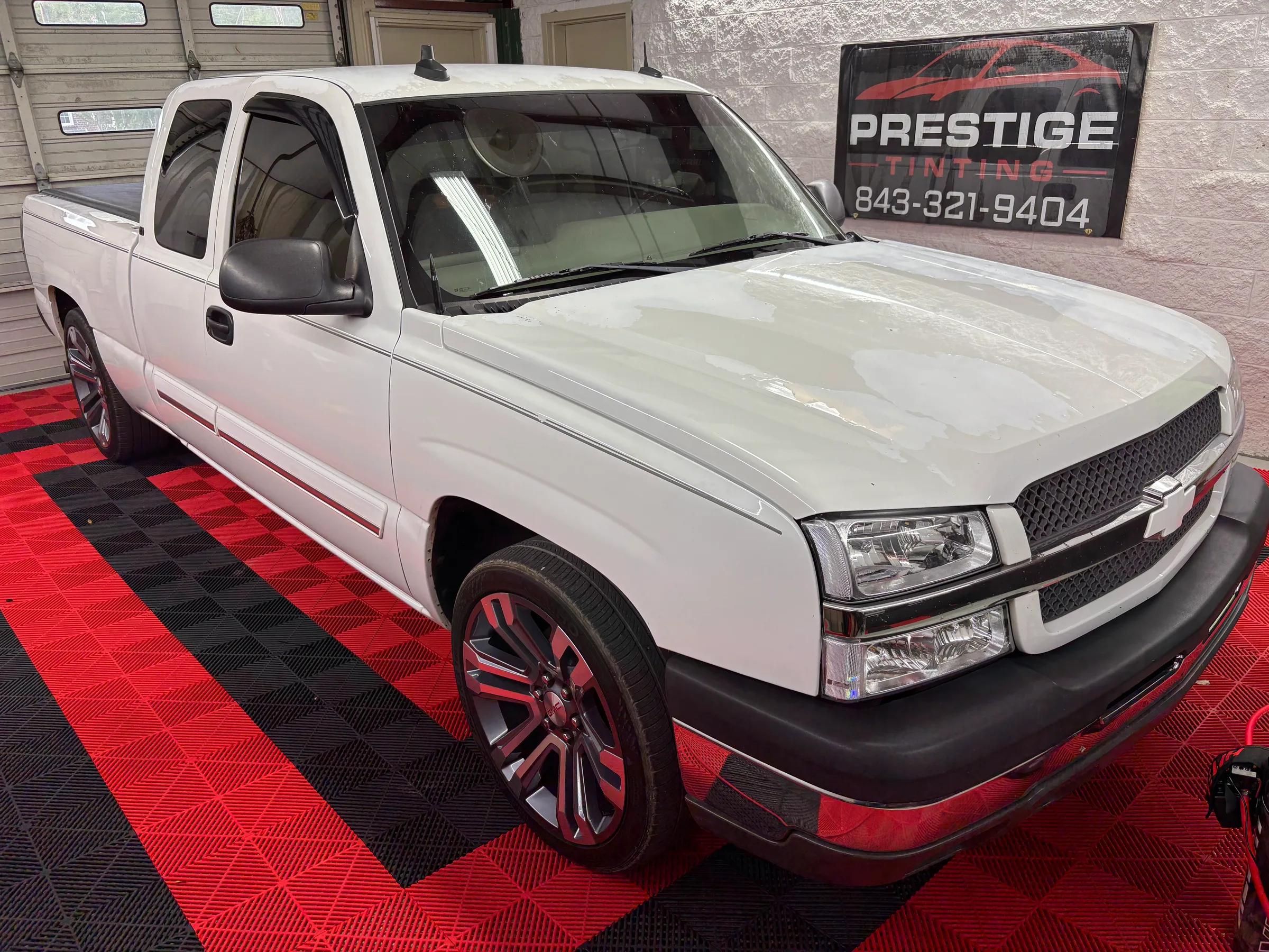 White Chevrolet Silverado with dark window tint displayed in a shop bay next to a Prestige Tinting sign.