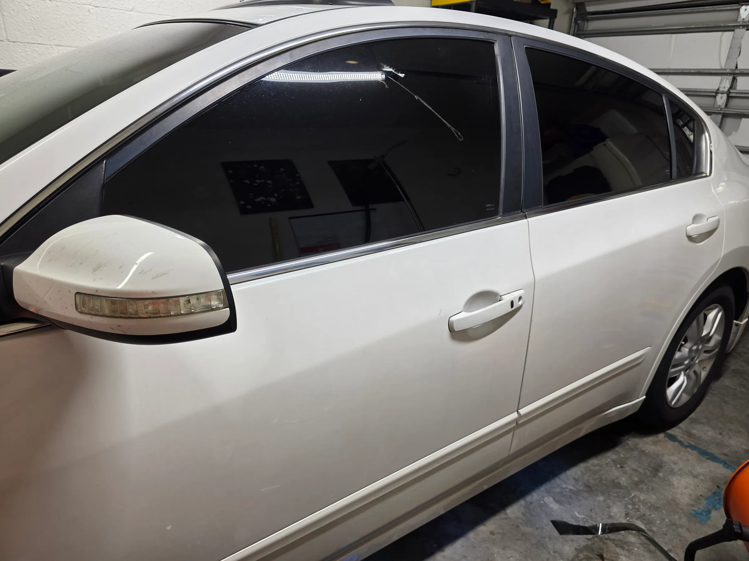 White sedan with dark window tint applied to the side windows, photographed in an indoor shop setting.