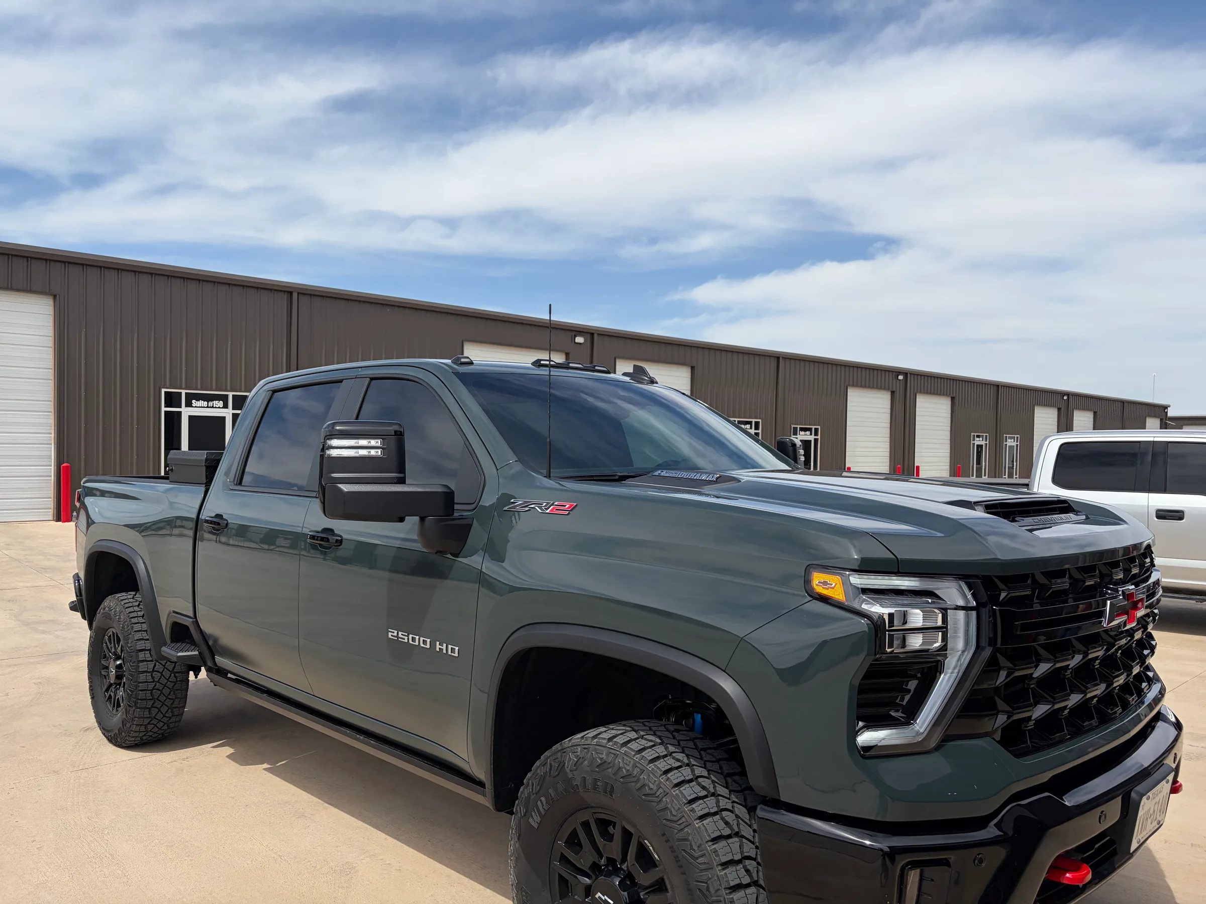 Front three-quarter view of a green Chevrolet Silverado 2500 HD with dark window tint applied to all windows, parked in front of an industrial building.