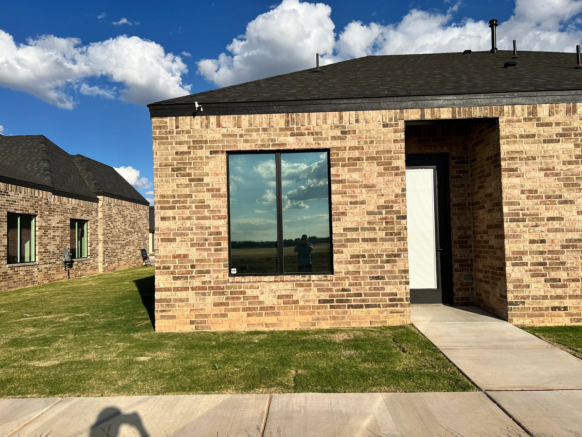A brick residential building with tinted windows reflecting the sky and clouds, demonstrating window film installation on a modern home exterior.
