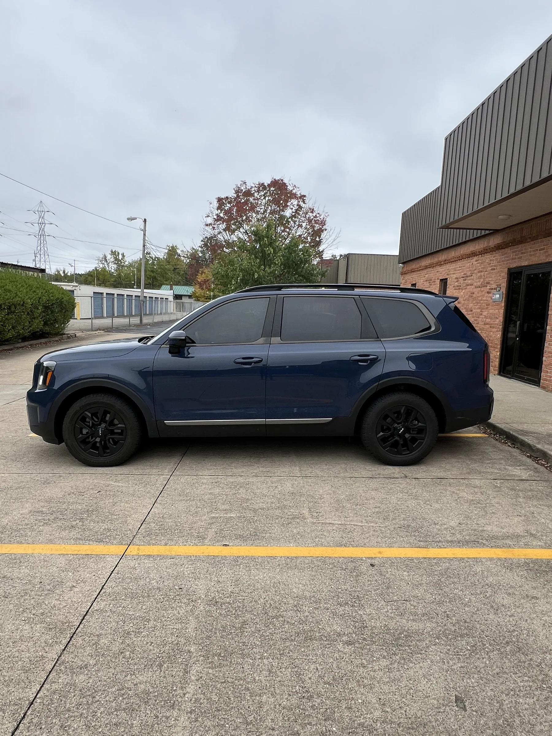 A blue Kia Telluride with tinted windows parked in front of a brick automotive shop in Berea, Ohio.