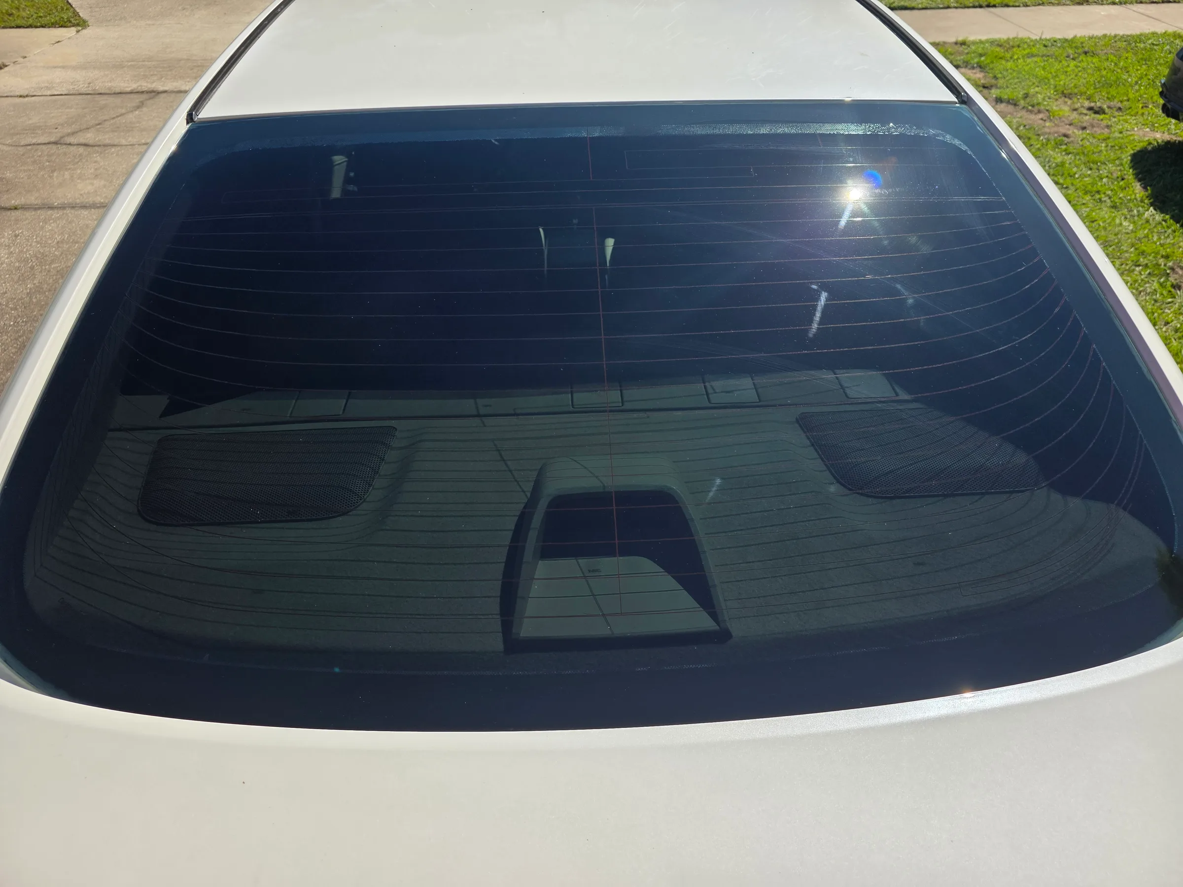 Rear window of a white sedan showing dark window tint applied to the glass with visible horizontal streaks from sun reflection.