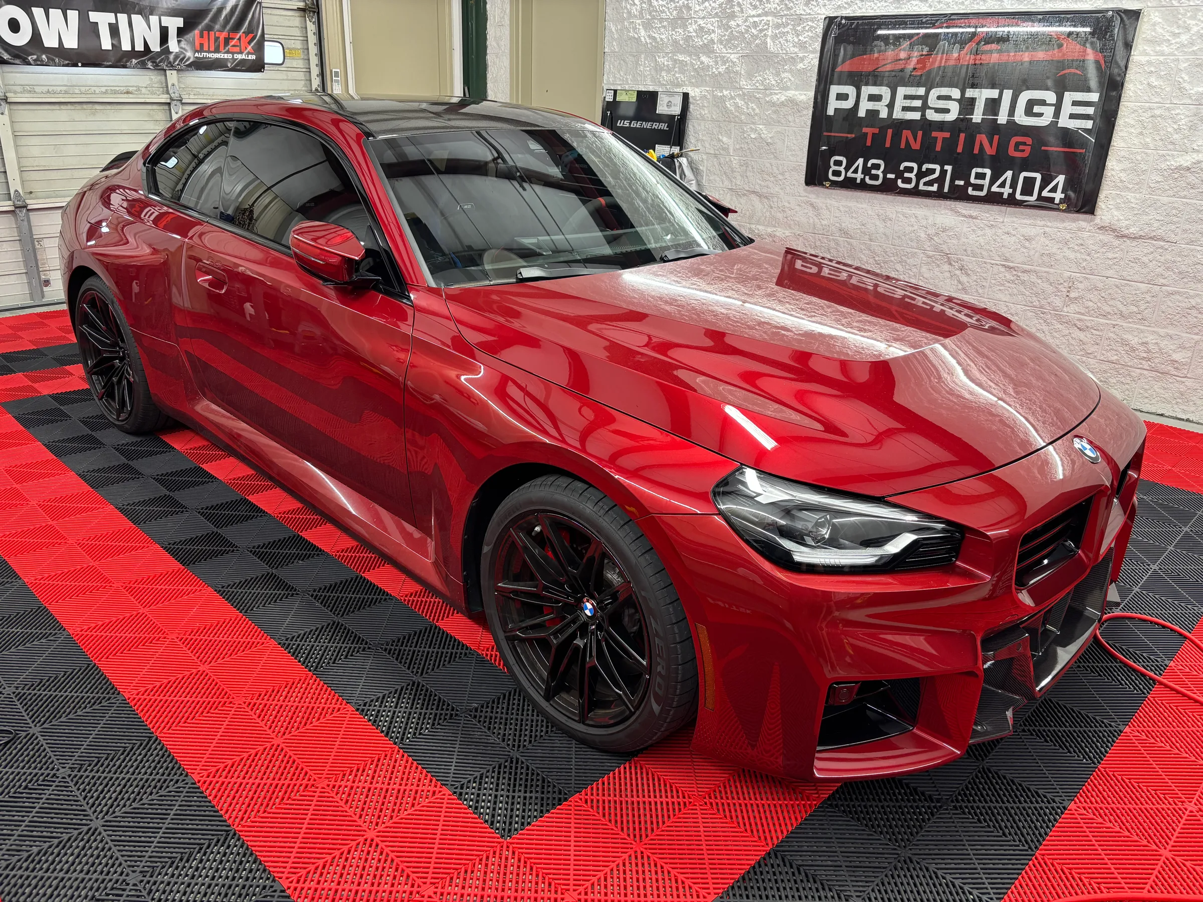 A bright red BMW with dark window tint applied to all windows, displayed in the Prestige Tinting shop in Conway, SC.