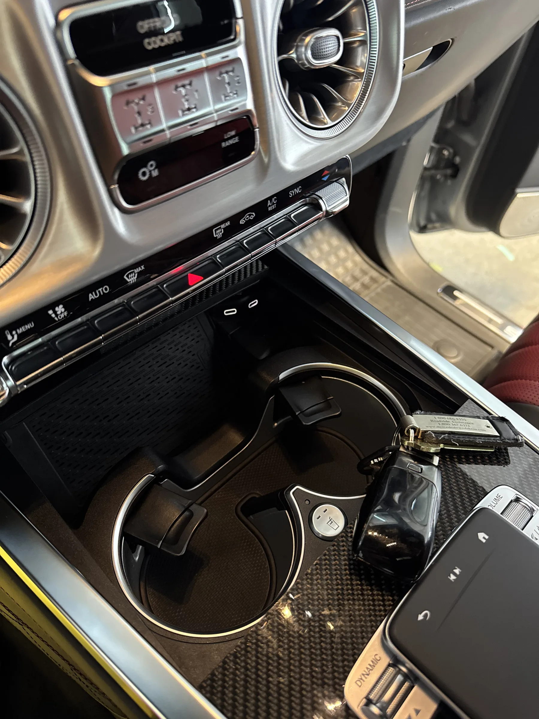 Close-up of a Mercedes-AMG interior showing the center console, steering wheel, and dashboard with protective film applied to the carbon fiber trim and cup holder area.