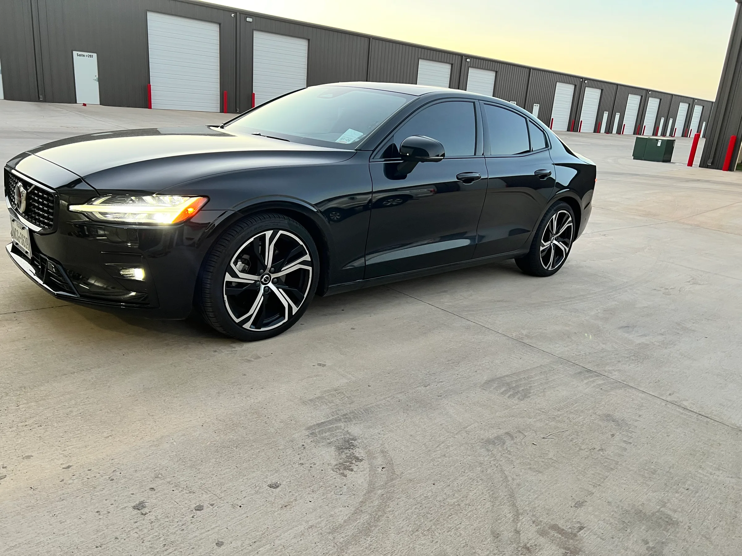 Black Volvo sedan with dark tinted windows parked in front of an industrial building.