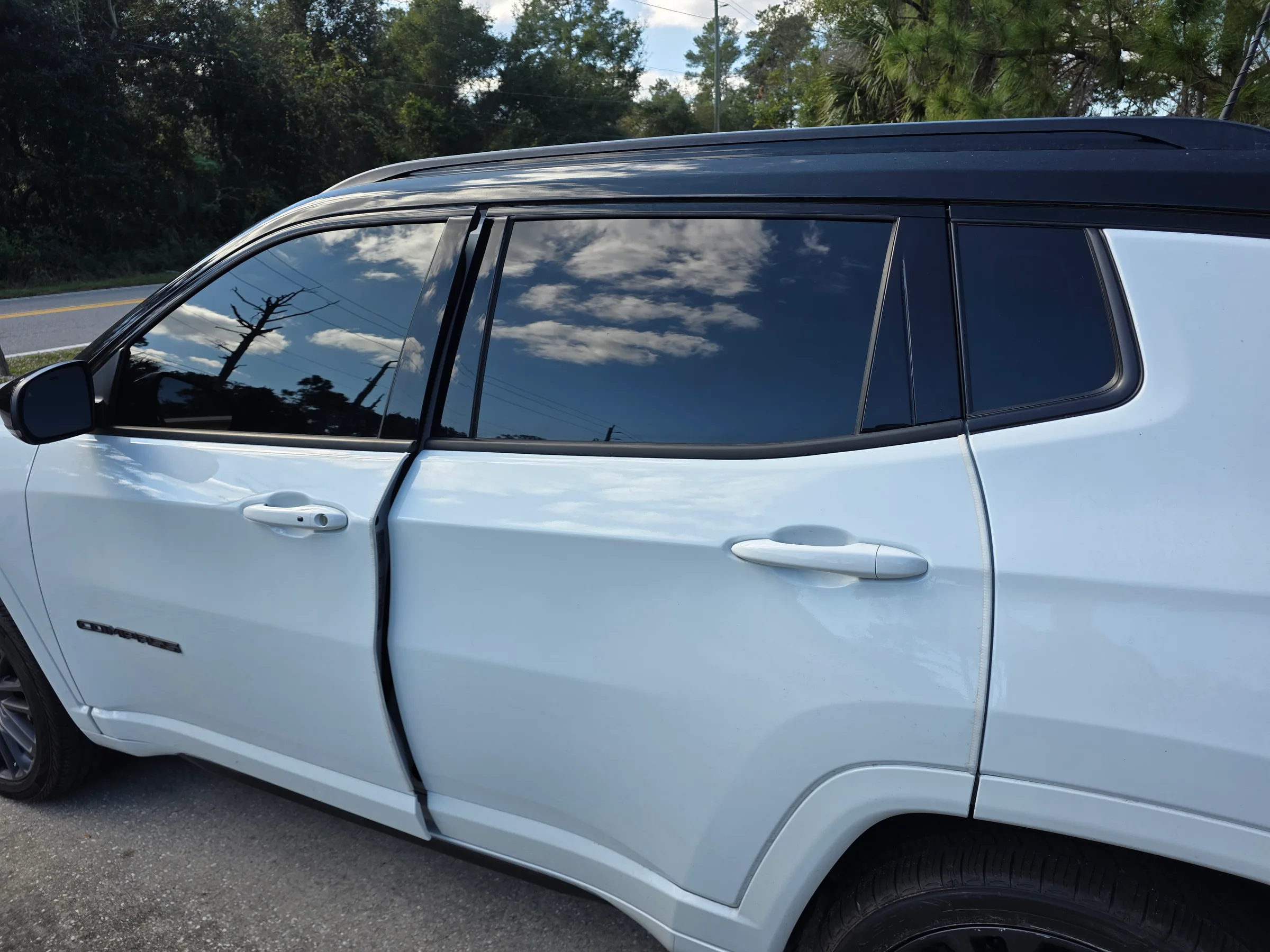 White SUV with dark window tint applied to the side windows, parked on a sunny day with trees visible in the background.