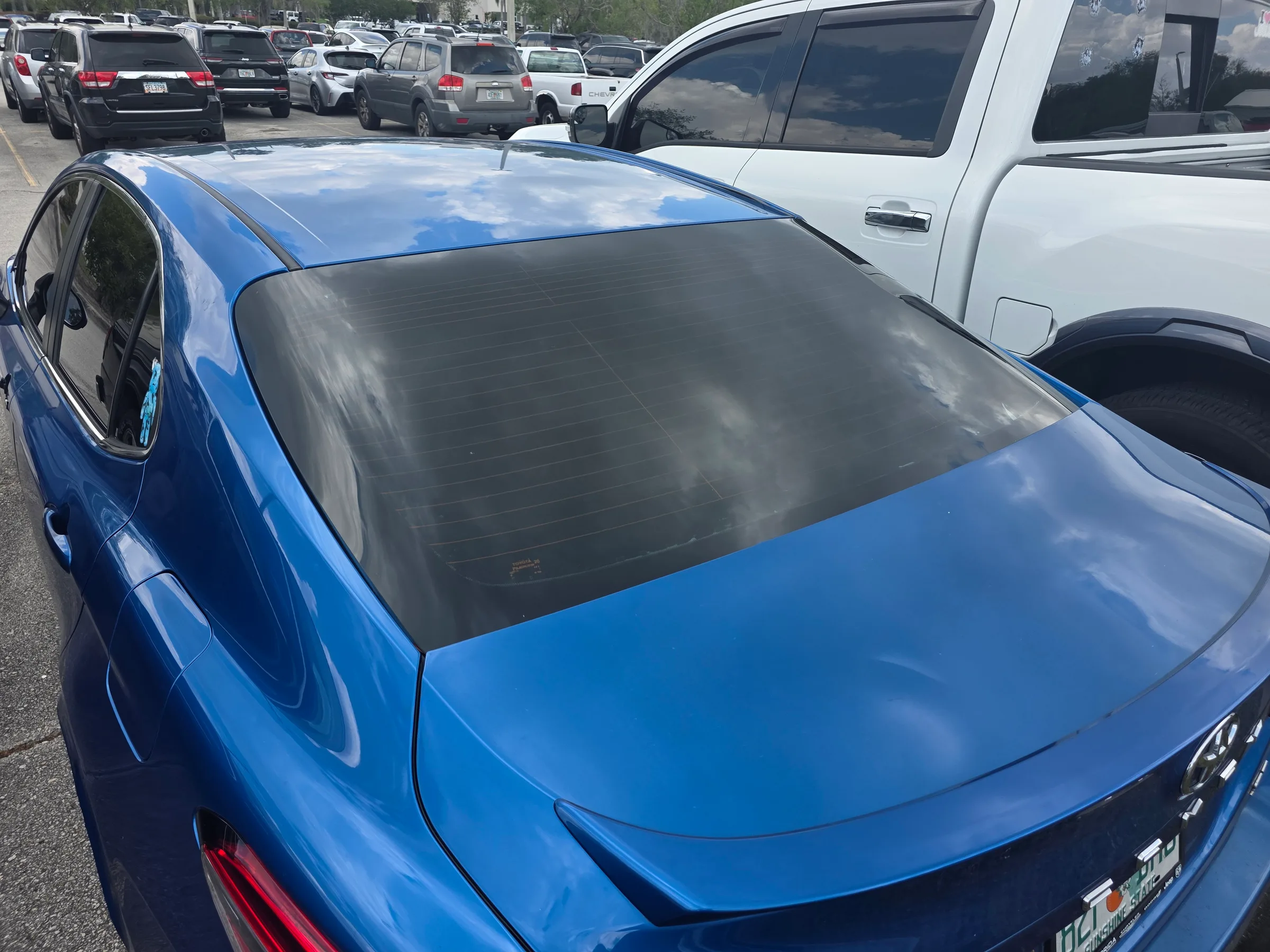 A blue sedan with a black tonneau cover installed on its bed, parked in a lot with other vehicles.