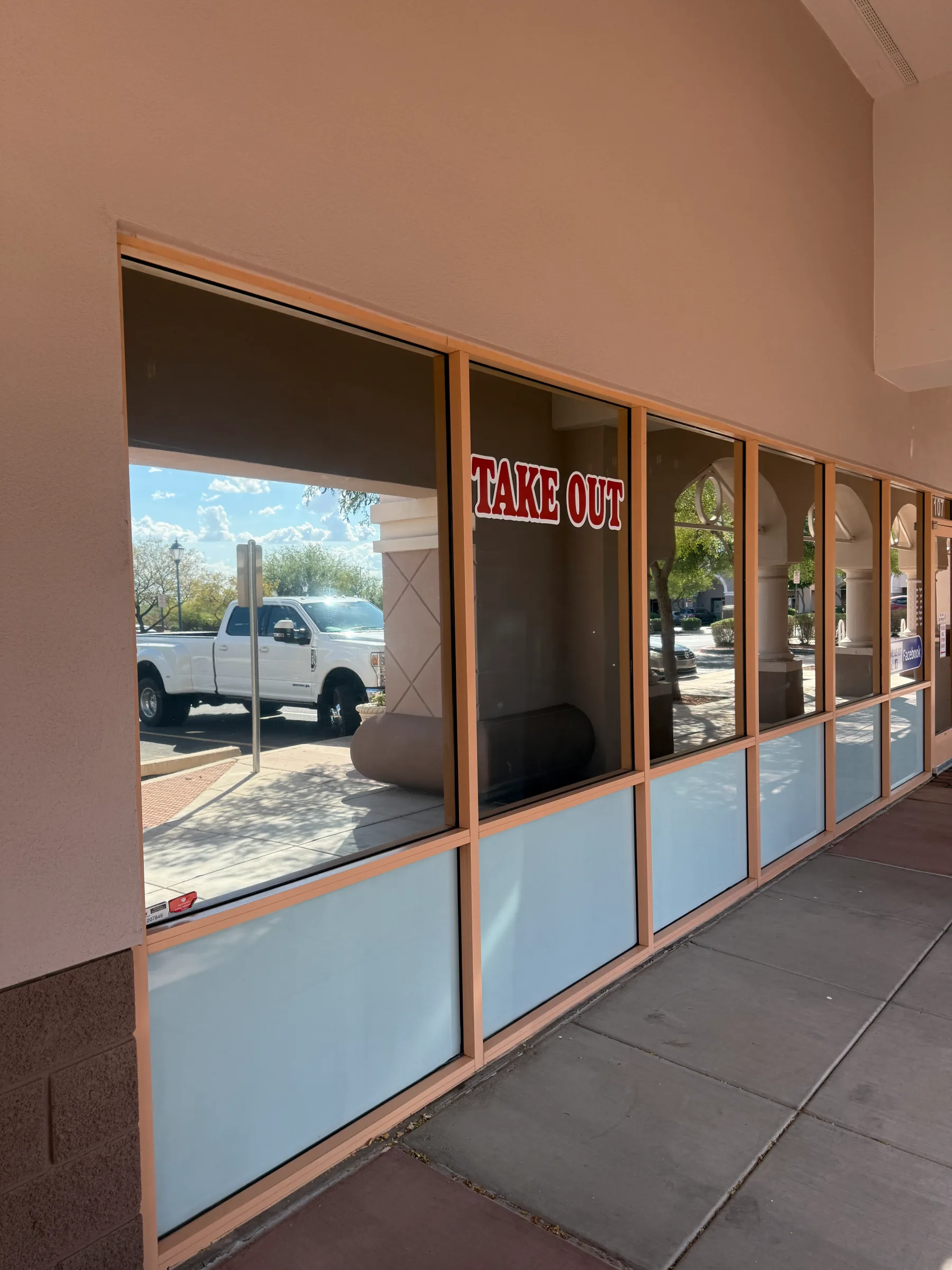 A storefront with tinted commercial windows and a takeout sign, showing a white pickup truck parked outside in Arizona.