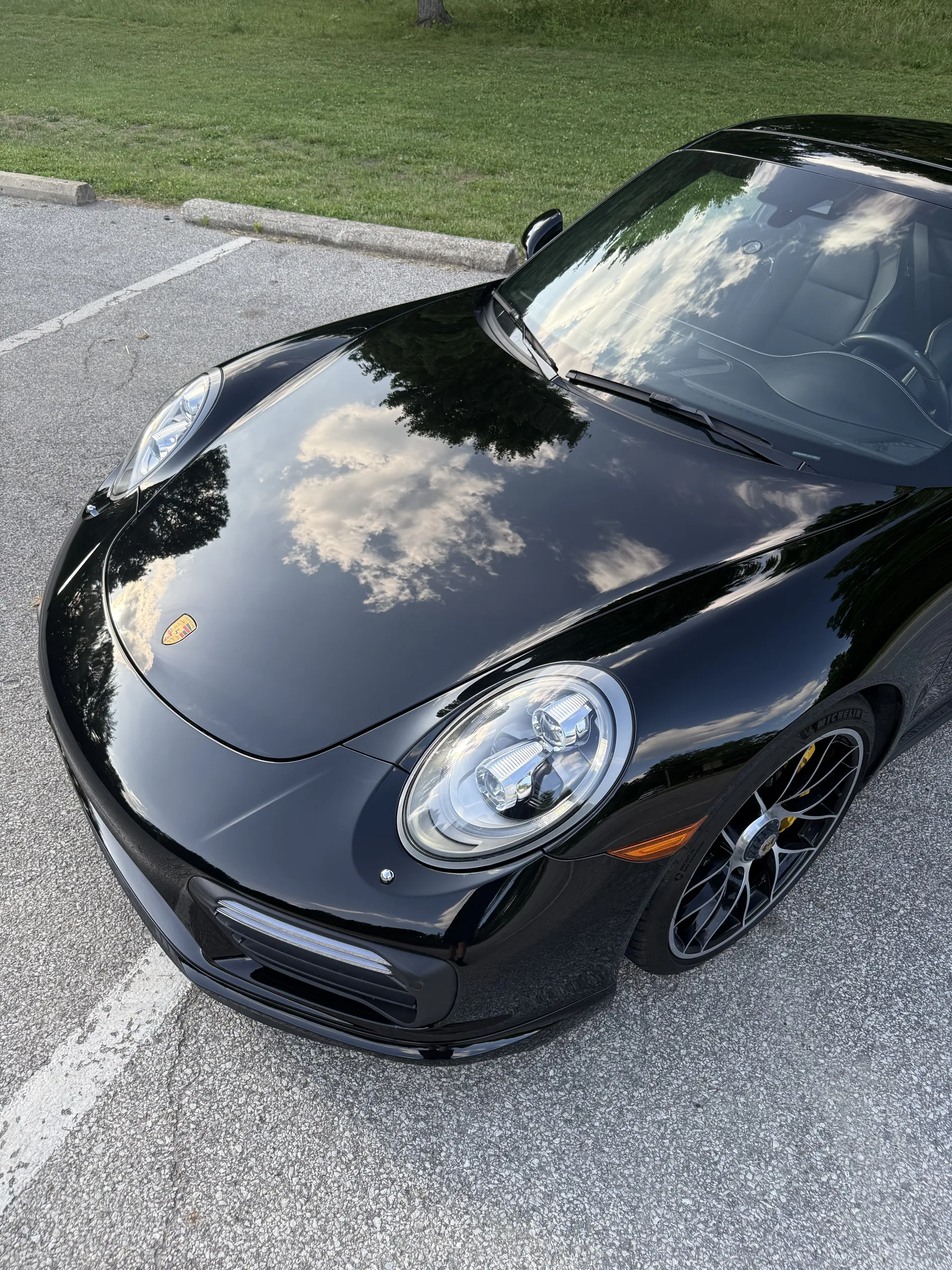 A black Porsche 911 with a pristine ceramic-coated finish, parked on asphalt with a grass lawn in the background.
