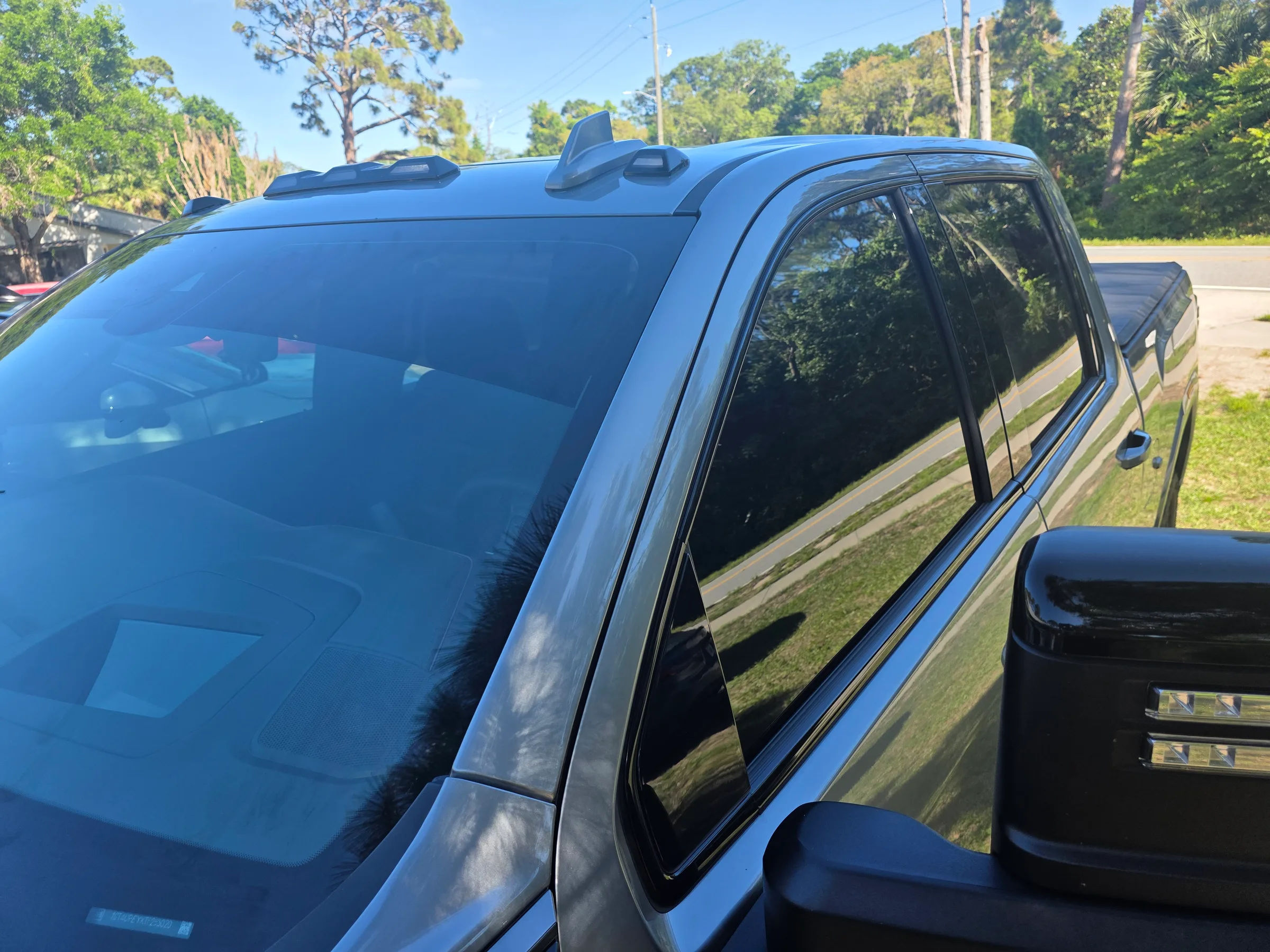 A blue pickup truck with dark window tint applied to the side and rear windows, parked outdoors with trees in the background.