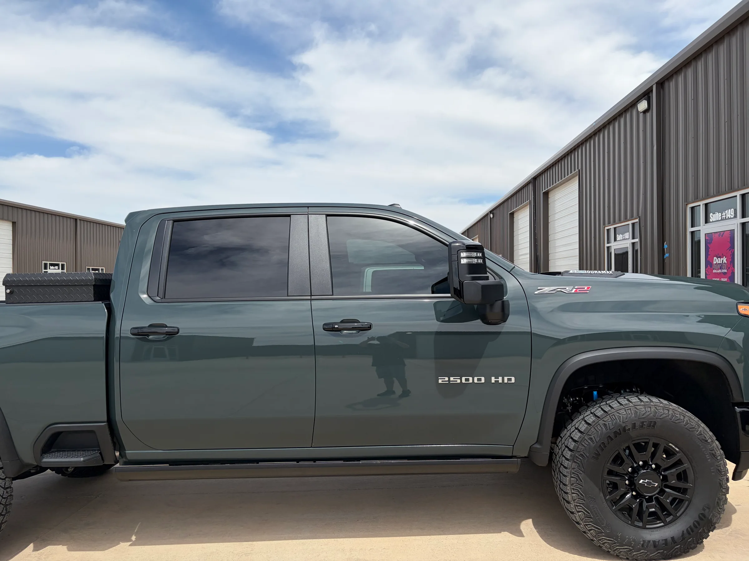 A green Chevrolet 2500 HD pickup truck with dark window tint applied to all windows, parked outside an automotive shop in Lubbock.