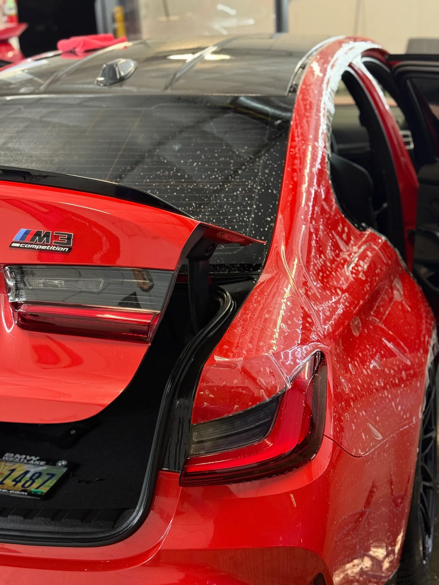Close-up of a red BMW M3 with paint protection film applied to the door edge and a black protective film visible on the roof.