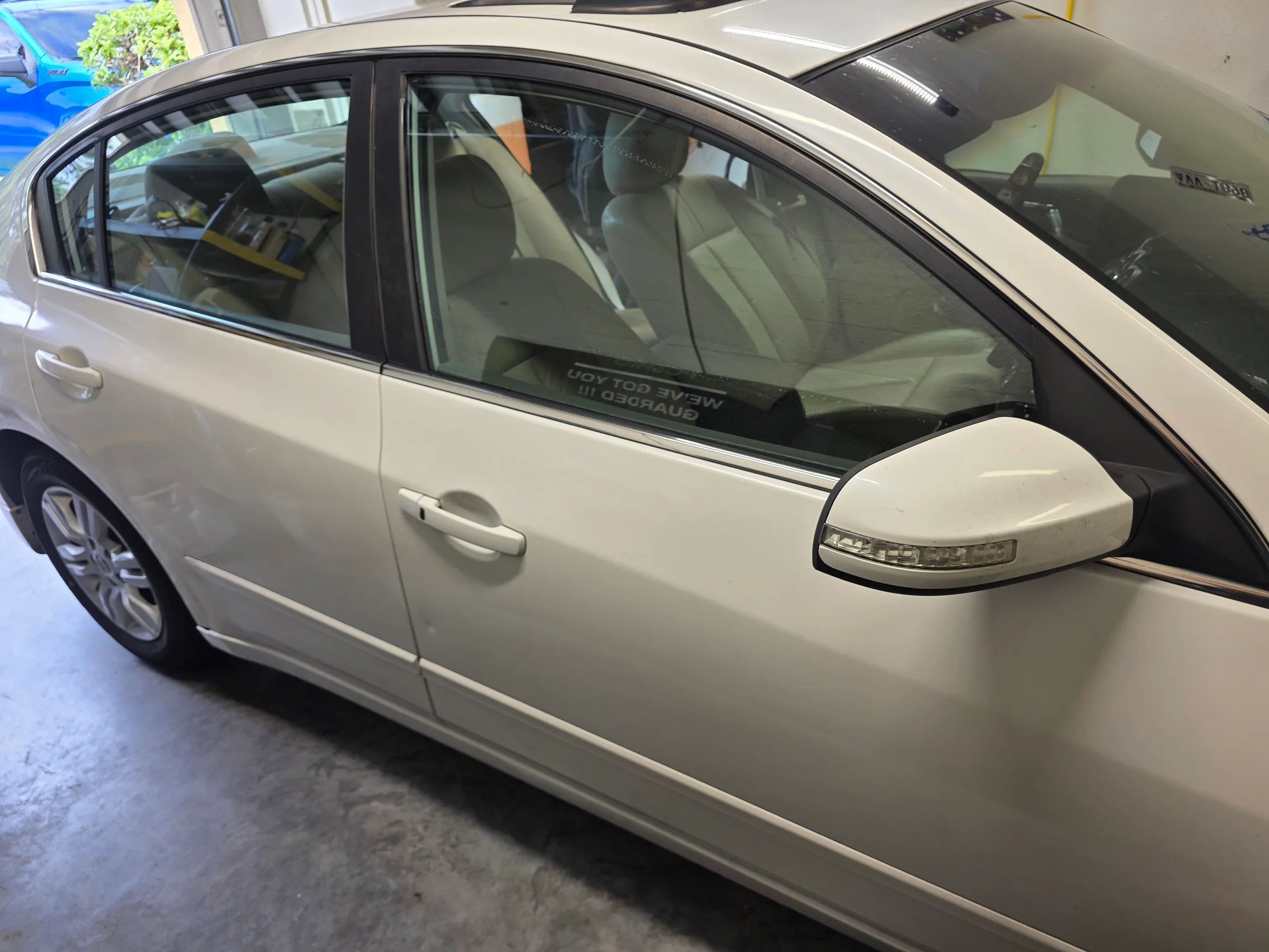 White sedan with dark window tint applied to the side windows, shown in an indoor service bay.