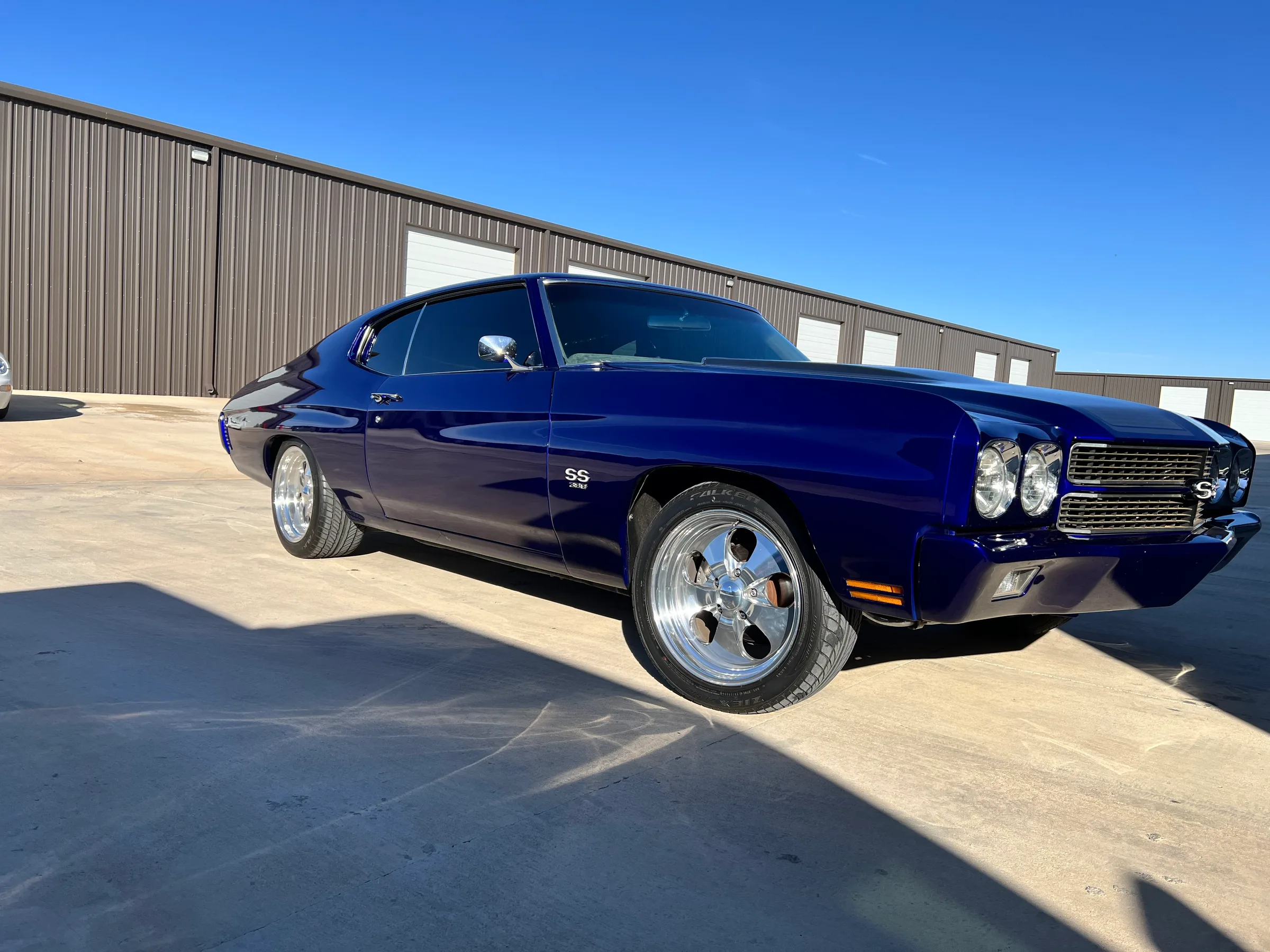 A deep blue Chevrolet Chevelle SS with tinted windows parked outside a metal warehouse building.