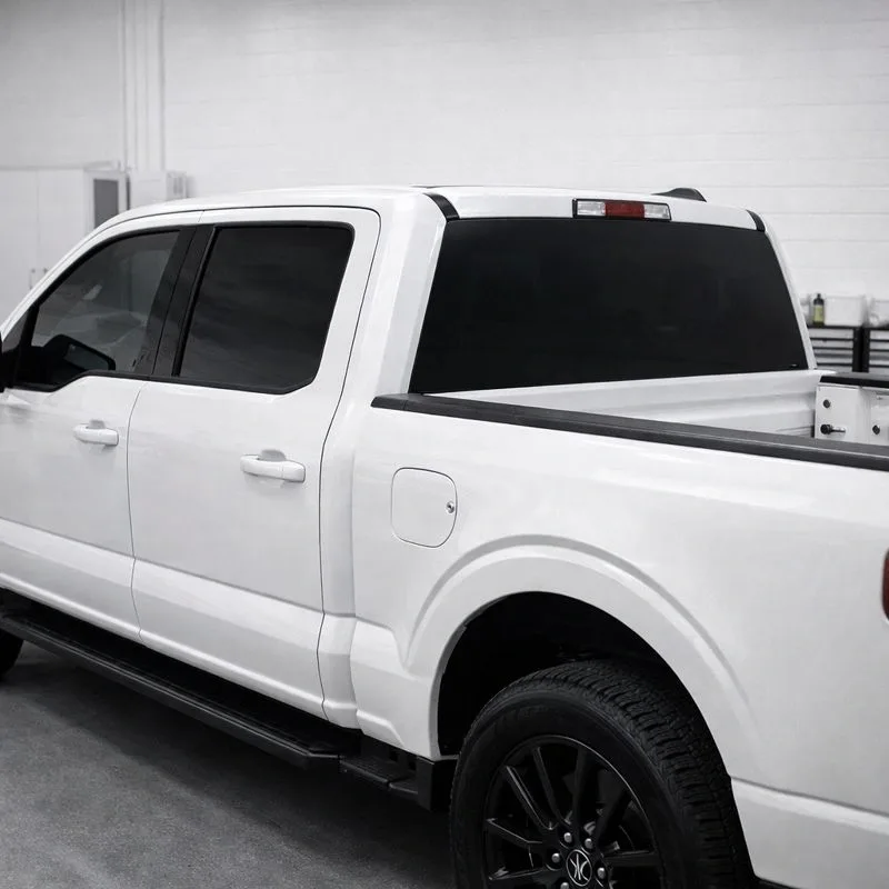 White pickup truck with dark window tint applied to the rear cab and rear window, photographed from the side in an indoor facility.