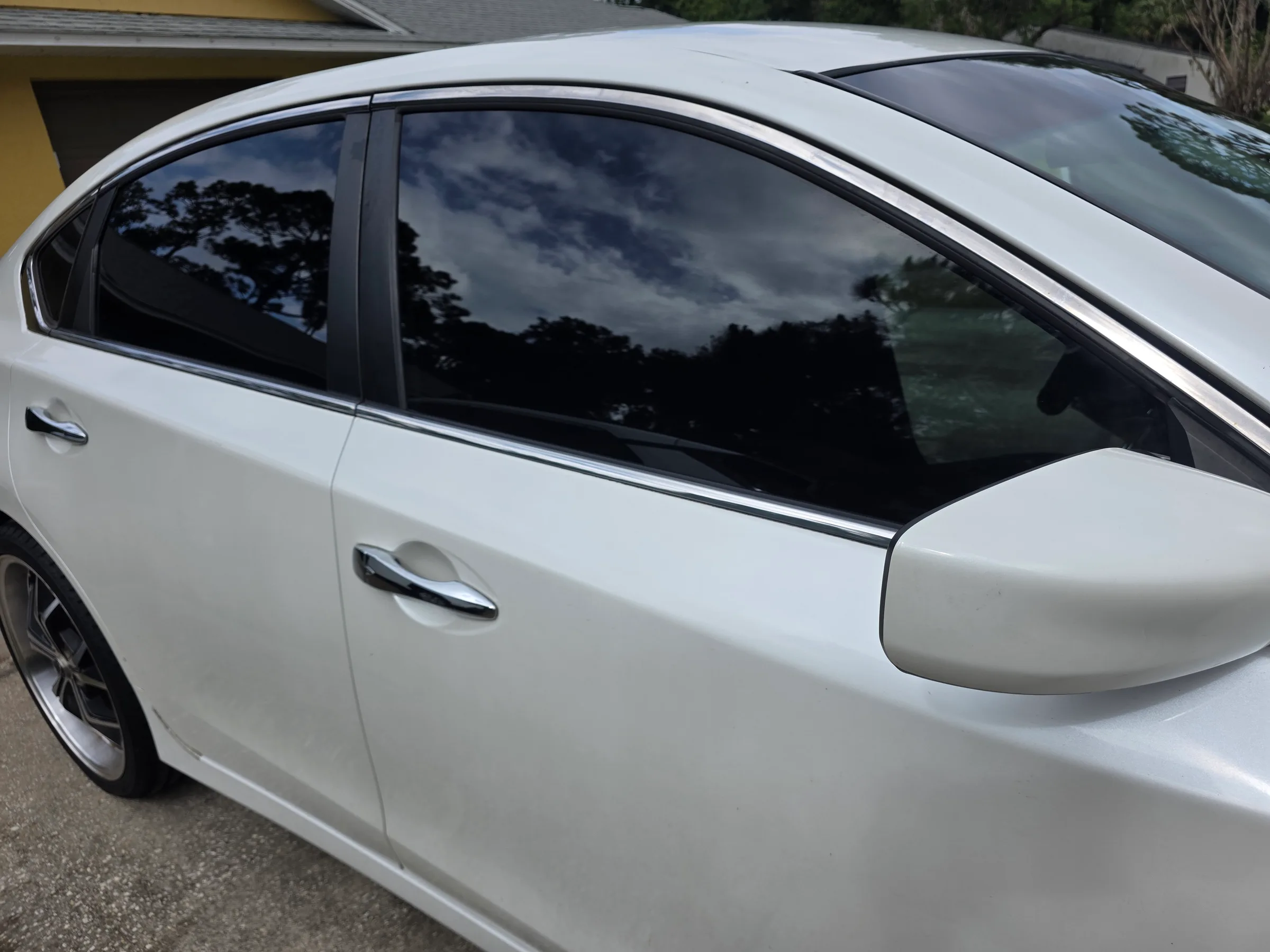 White sedan with dark window tint applied to the front and rear doors, showcasing the tinting service.