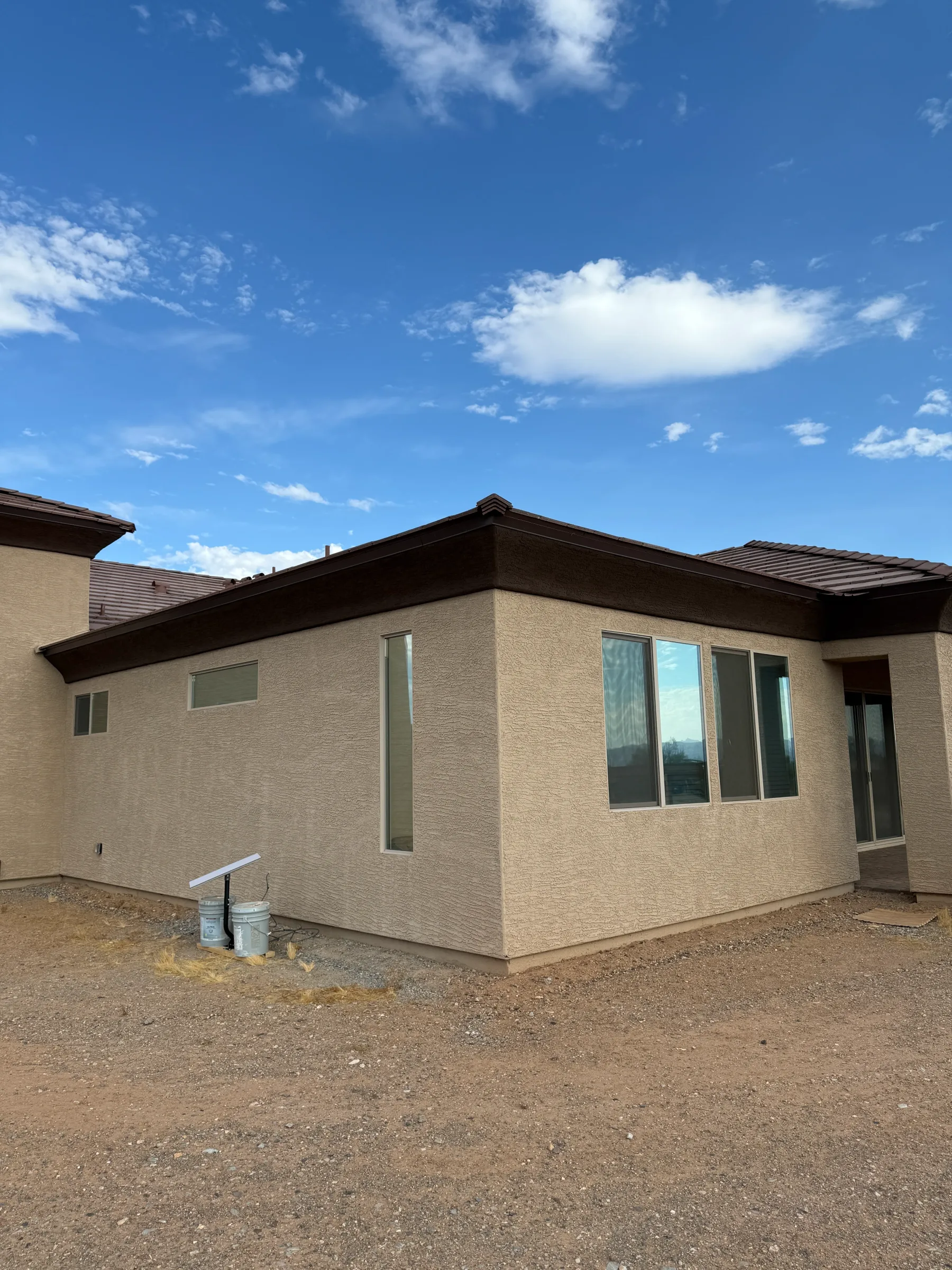 A modern tan brick residential home with large windows and dark roof trim in Cave Creek, Arizona on a clear sunny day.
