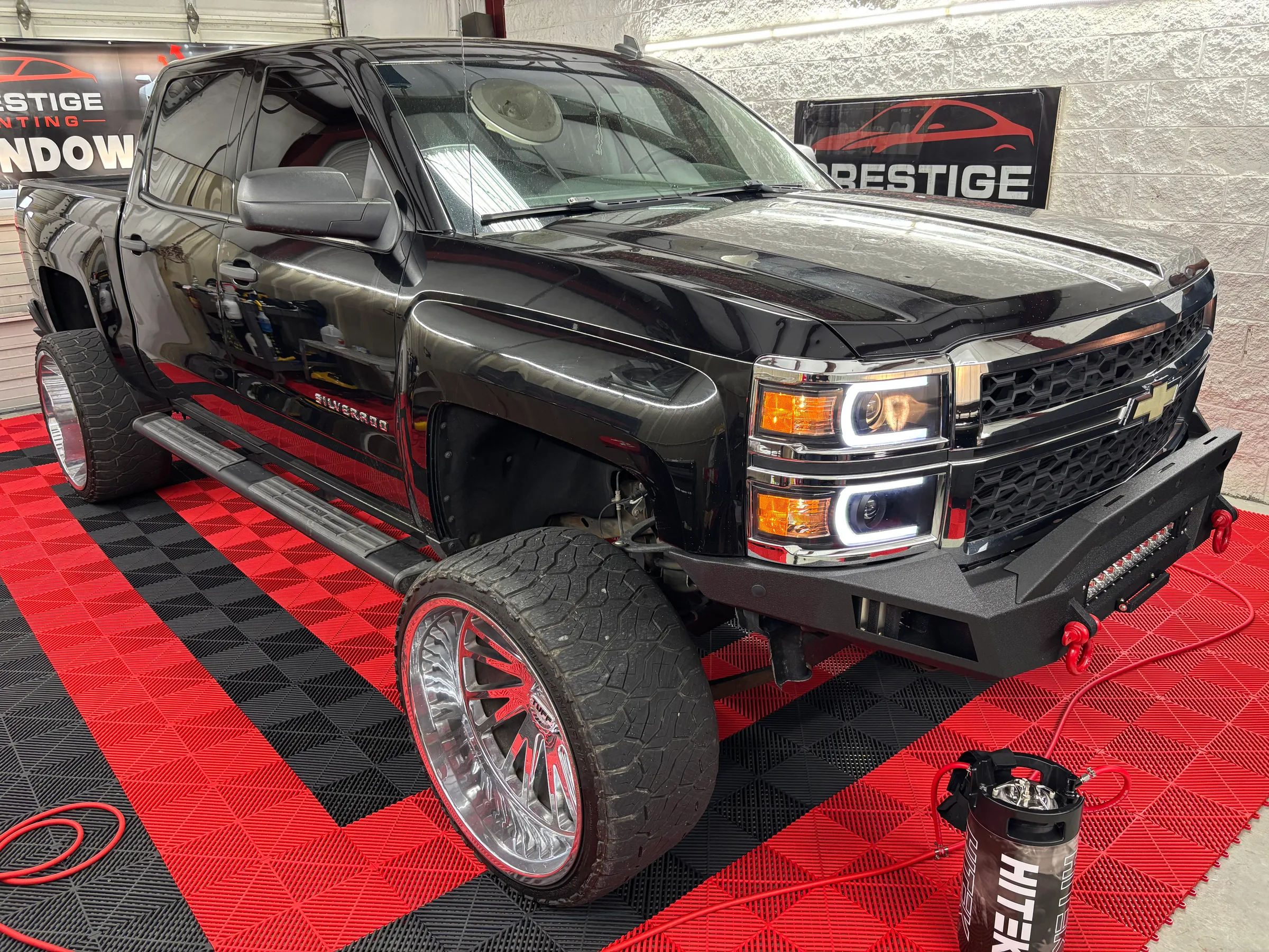A black Chevrolet Silverado with tinted windows displayed in a showroom with red and black flooring and Prestige Tinting signage.