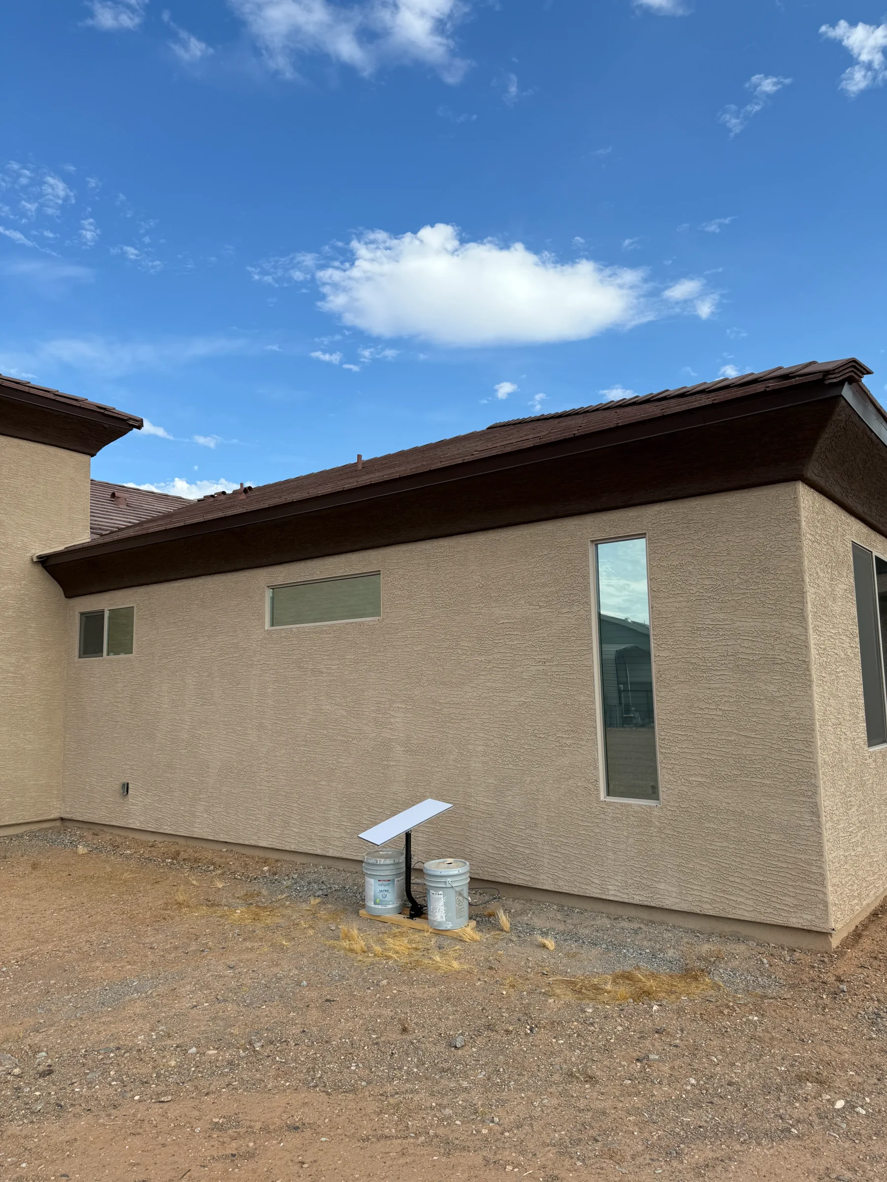 A tan brick residential home with tinted windows against a blue sky with white clouds.