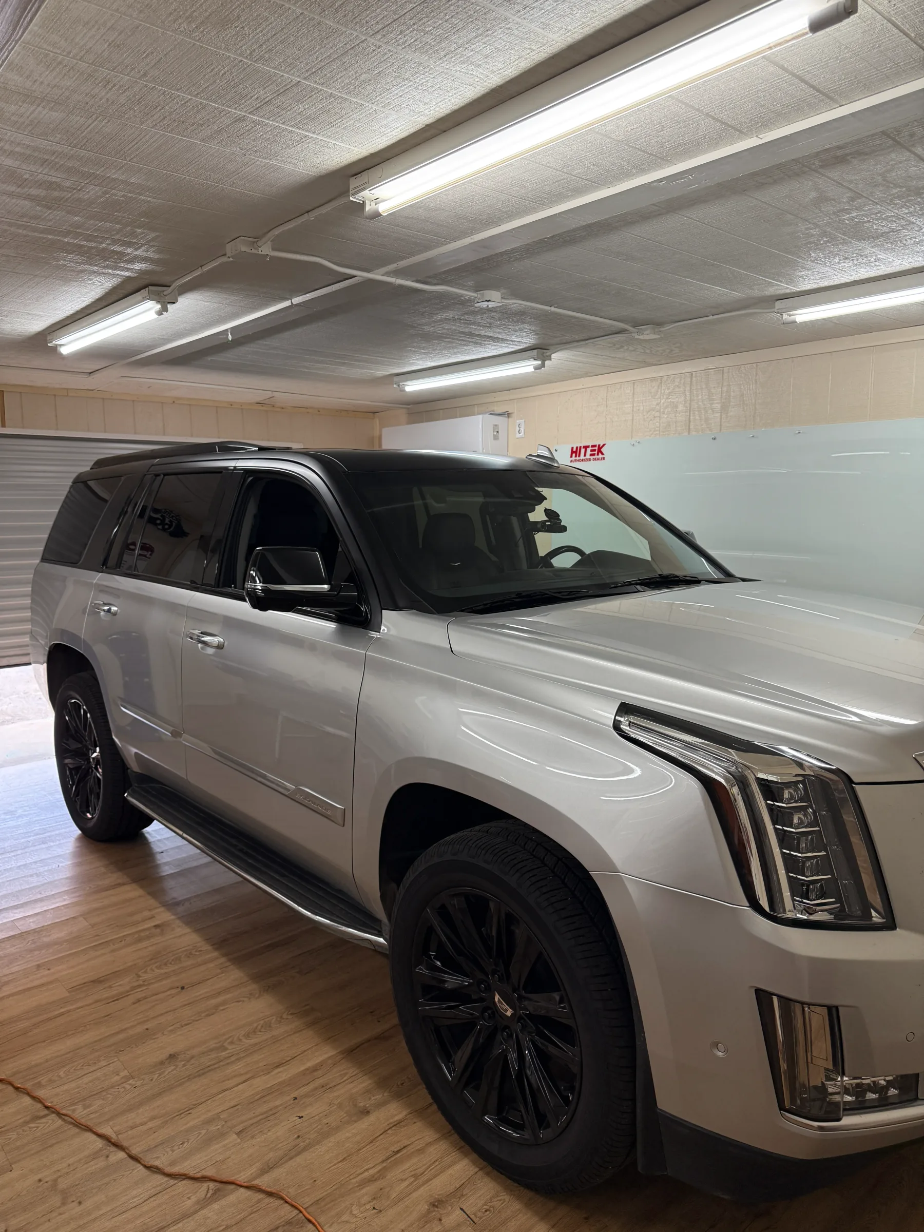 White Cadillac Escalade with dark window tint applied to the rear and side windows, parked in an indoor workshop with fluorescent lighting.