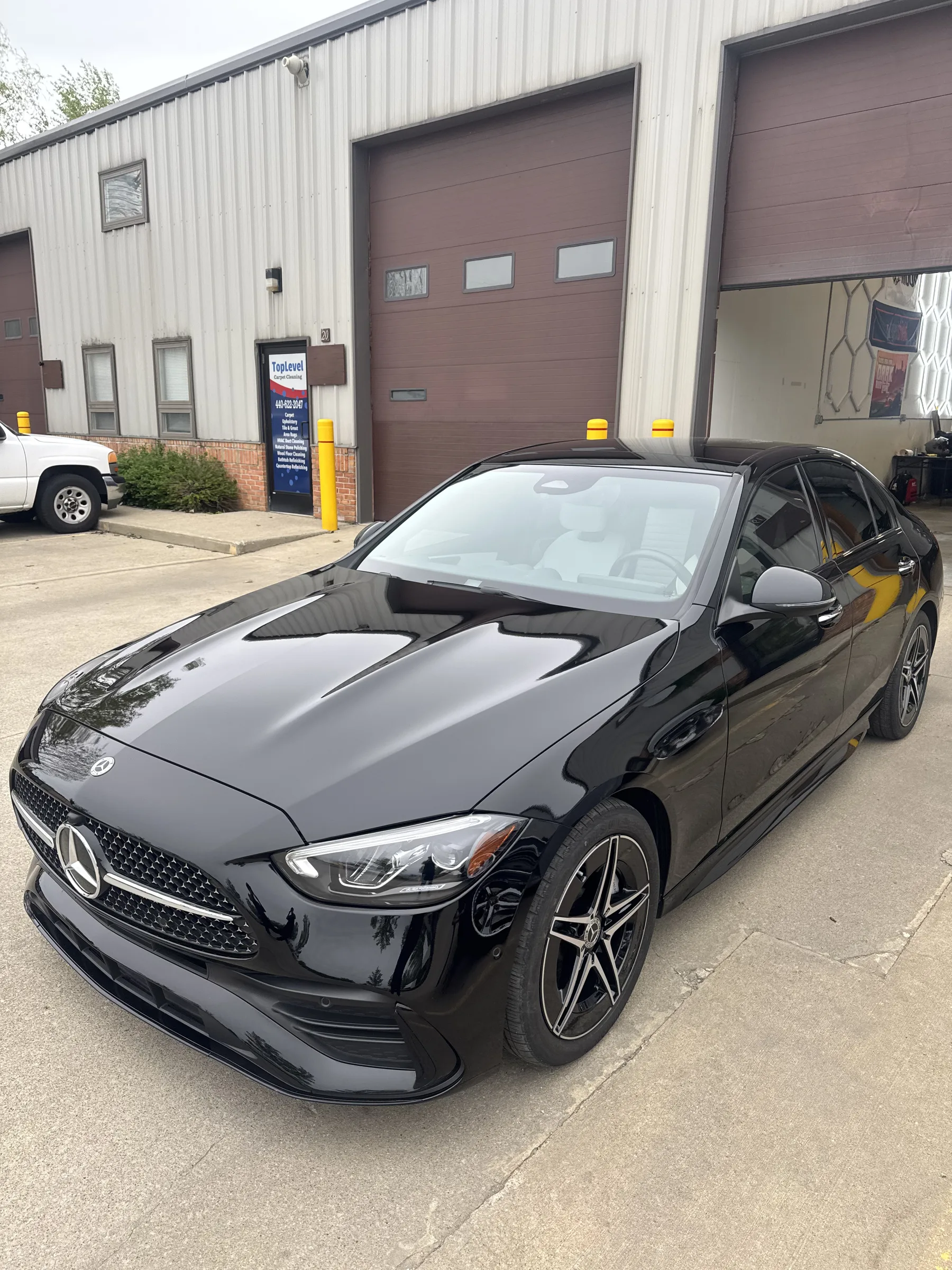 A black Mercedes-Benz C-Class sedan with paint protection film and a gray hood stripe parked outside an automotive shop in Berea, Ohio.