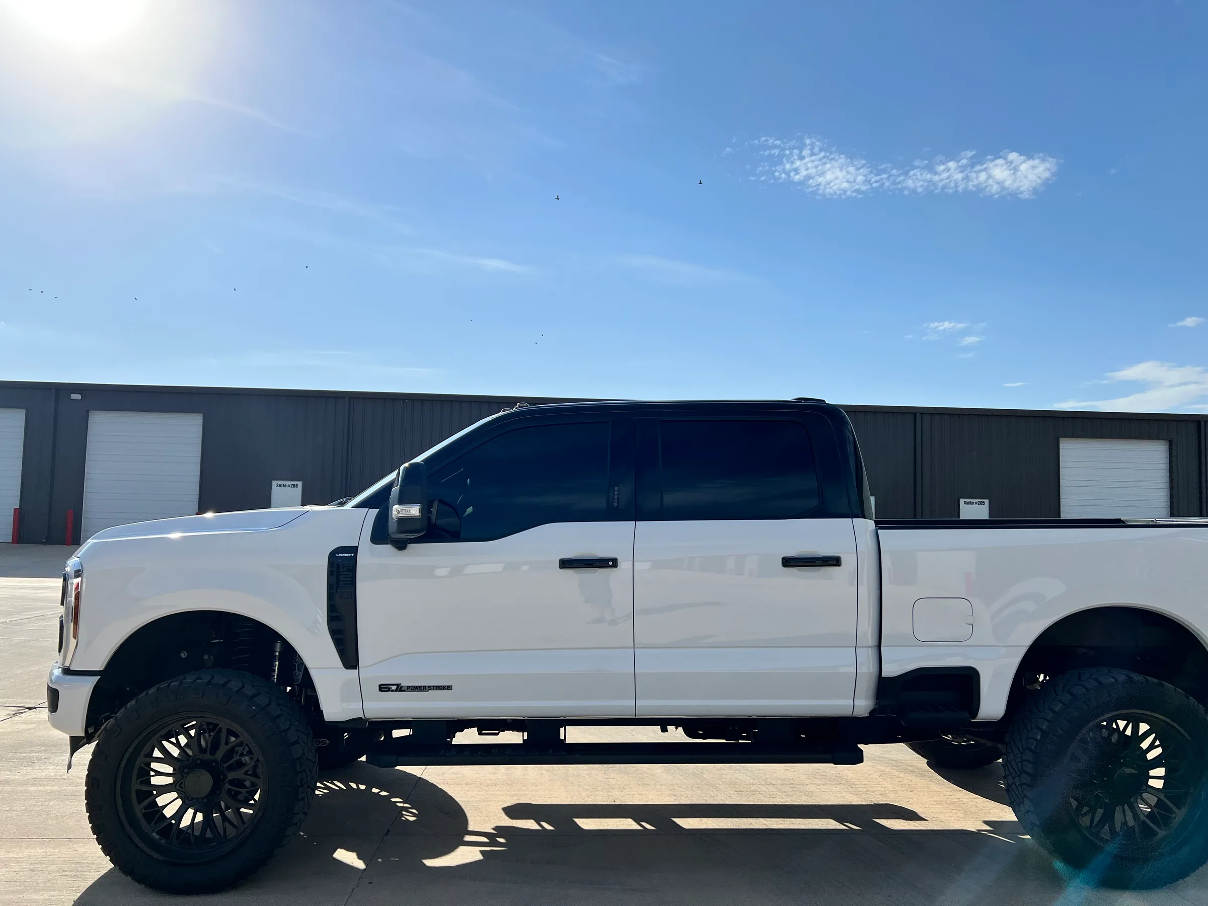 A lifted white and black Ford F-250 truck with dark tinted windows and custom wheels parked at a shop in Lubbock, Texas.