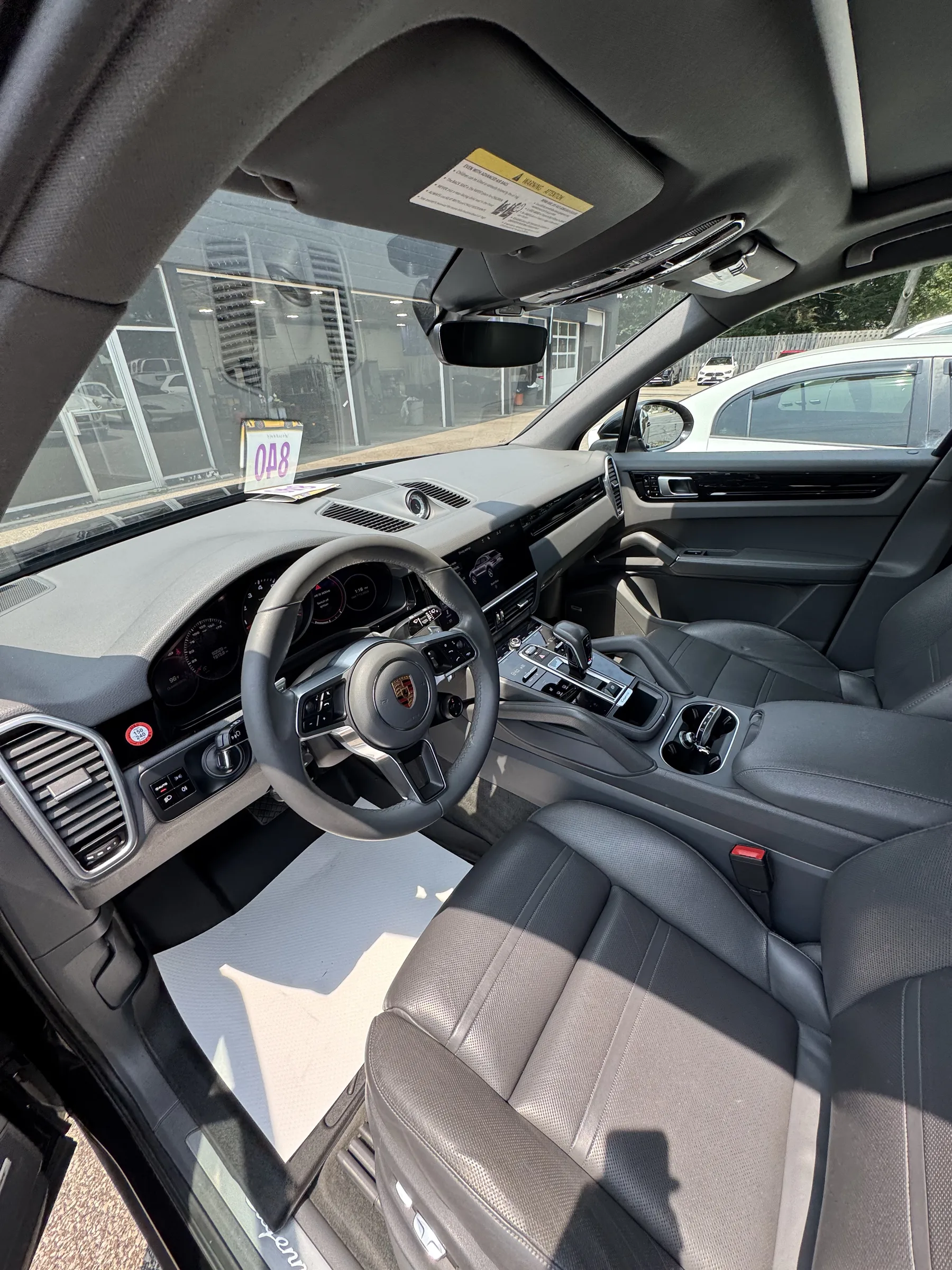 Interior view of a Porsche with dark-tinted front windows and a light gray and black leather cabin.