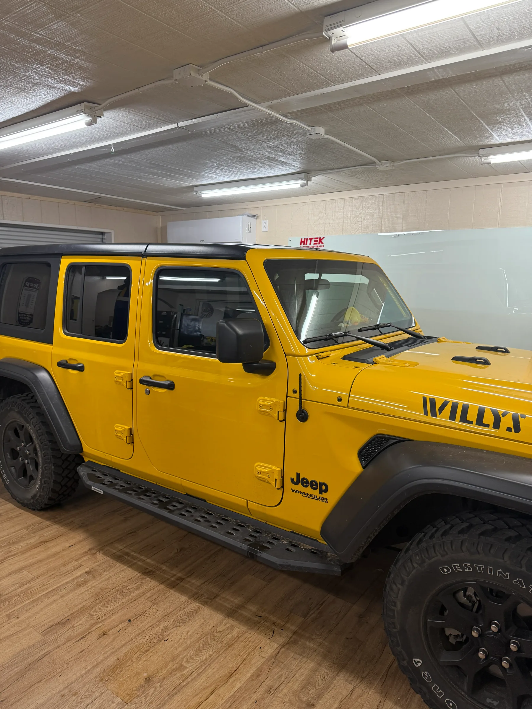 A bright yellow Jeep Wrangler with tinted windows parked in an indoor service bay at a tinting facility.