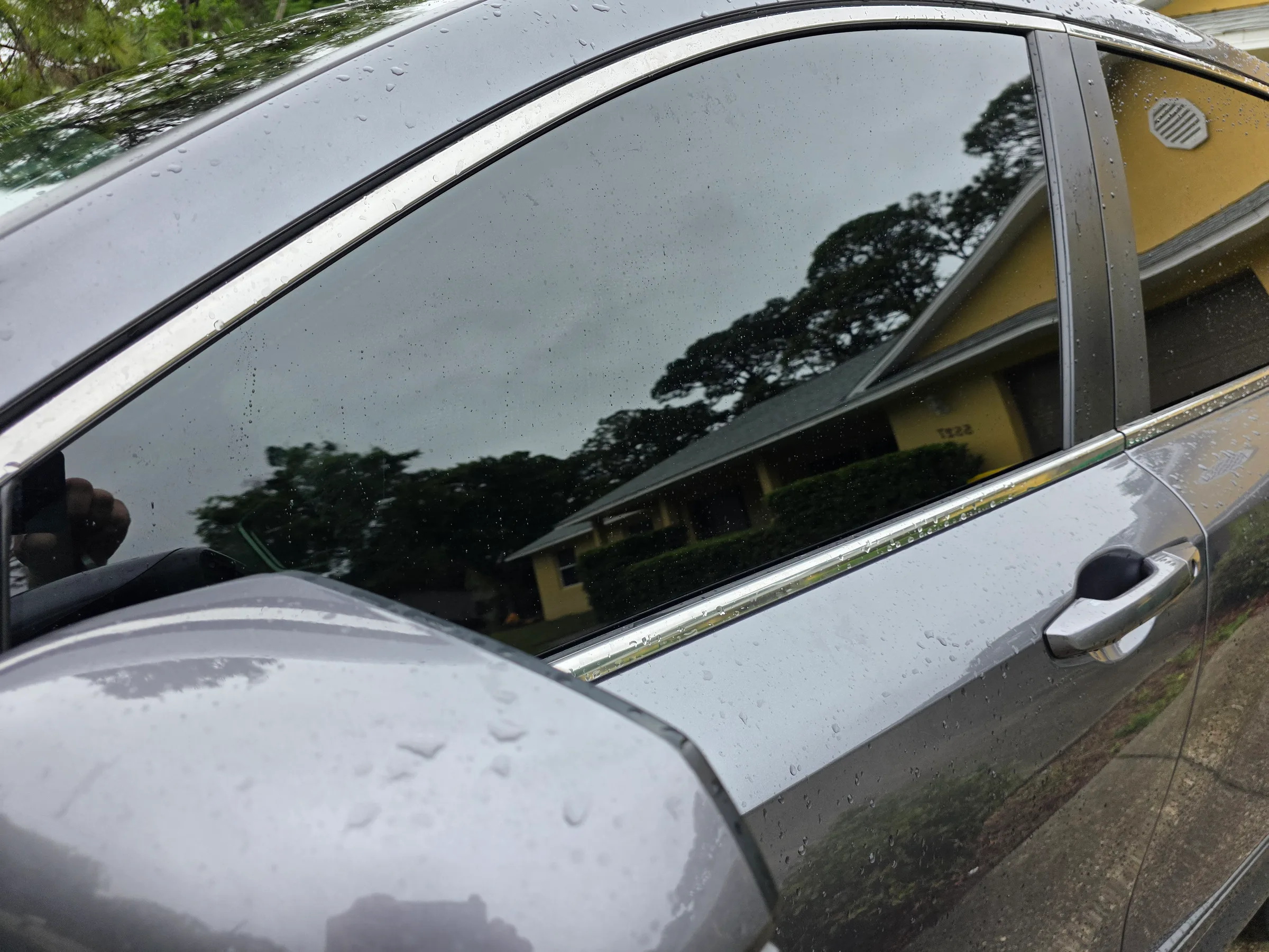 Close-up of a silver sedan with dark window tint applied to the side windows, showcasing the tint's heat-rejection and privacy properties on a wet day.