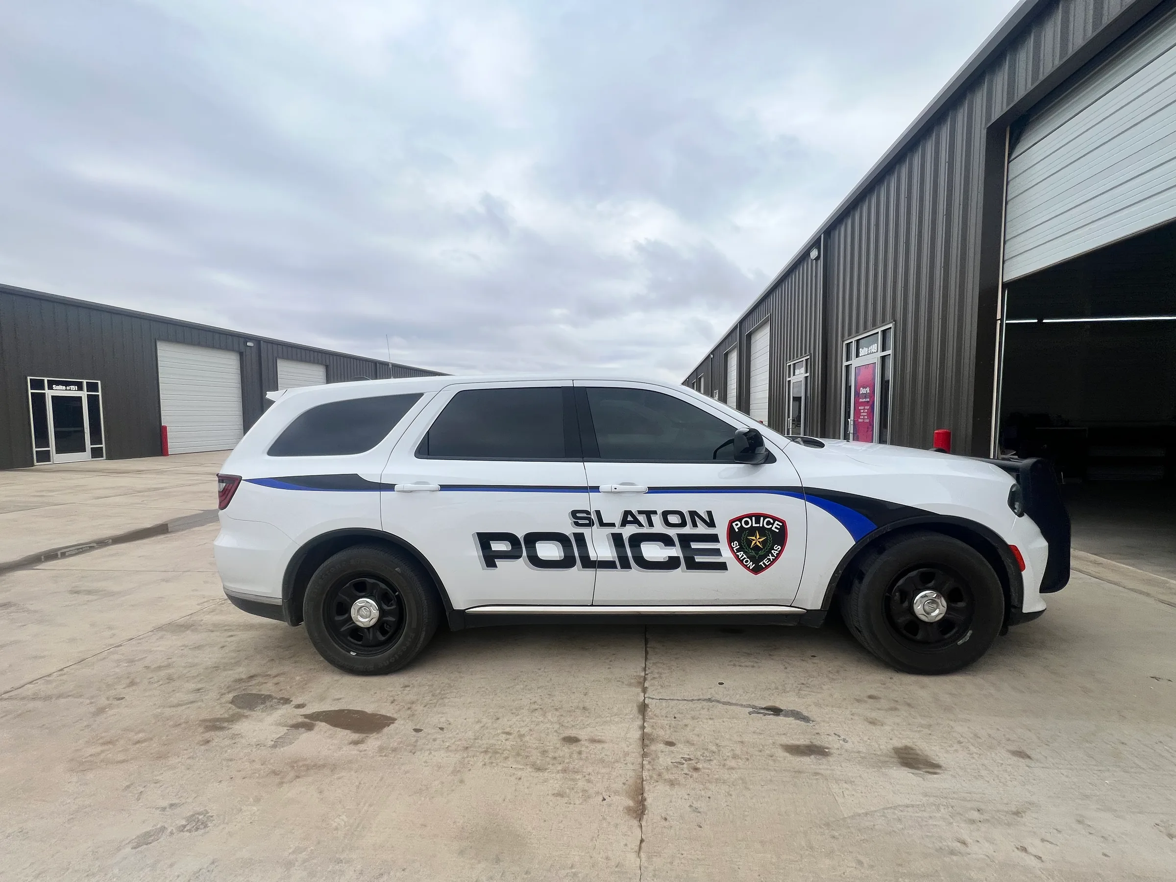 White and blue Slaton Police SUV with darkly tinted windows parked outside an industrial facility.