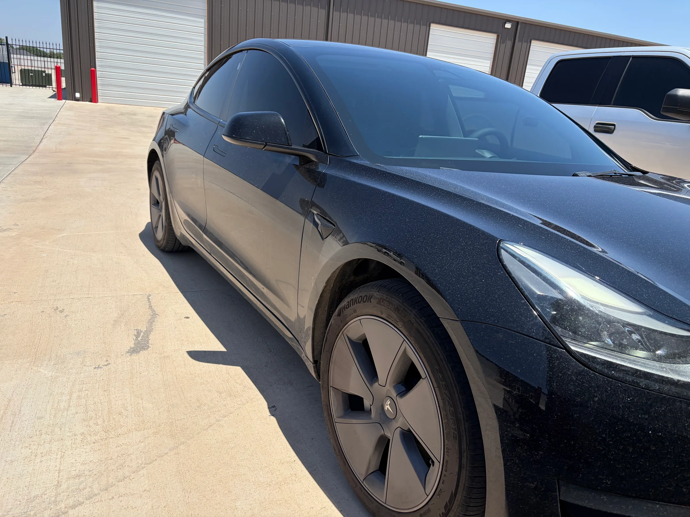 Black Tesla with dark window tint applied, shown from the front three-quarter angle in a service bay parking lot.