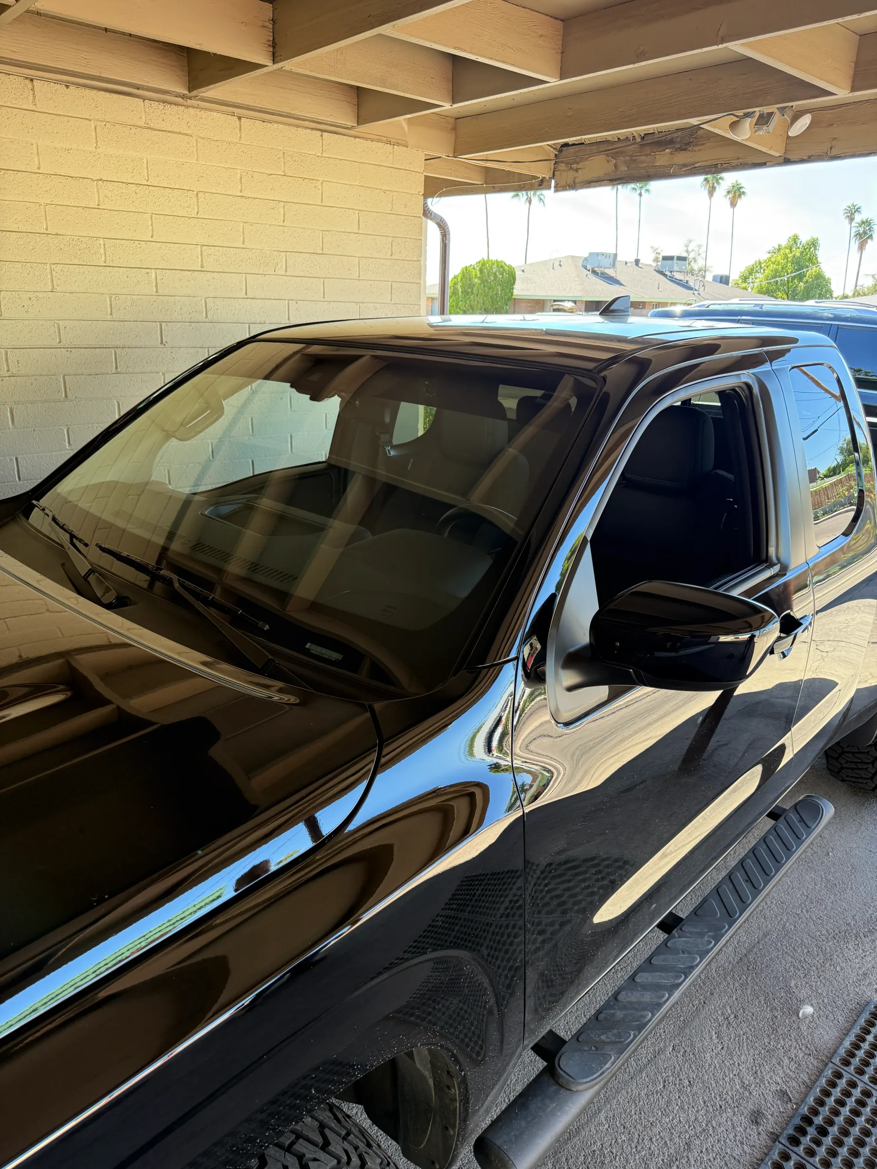A black pickup truck with dark window tint applied to the front and side windows, parked under a covered service bay.