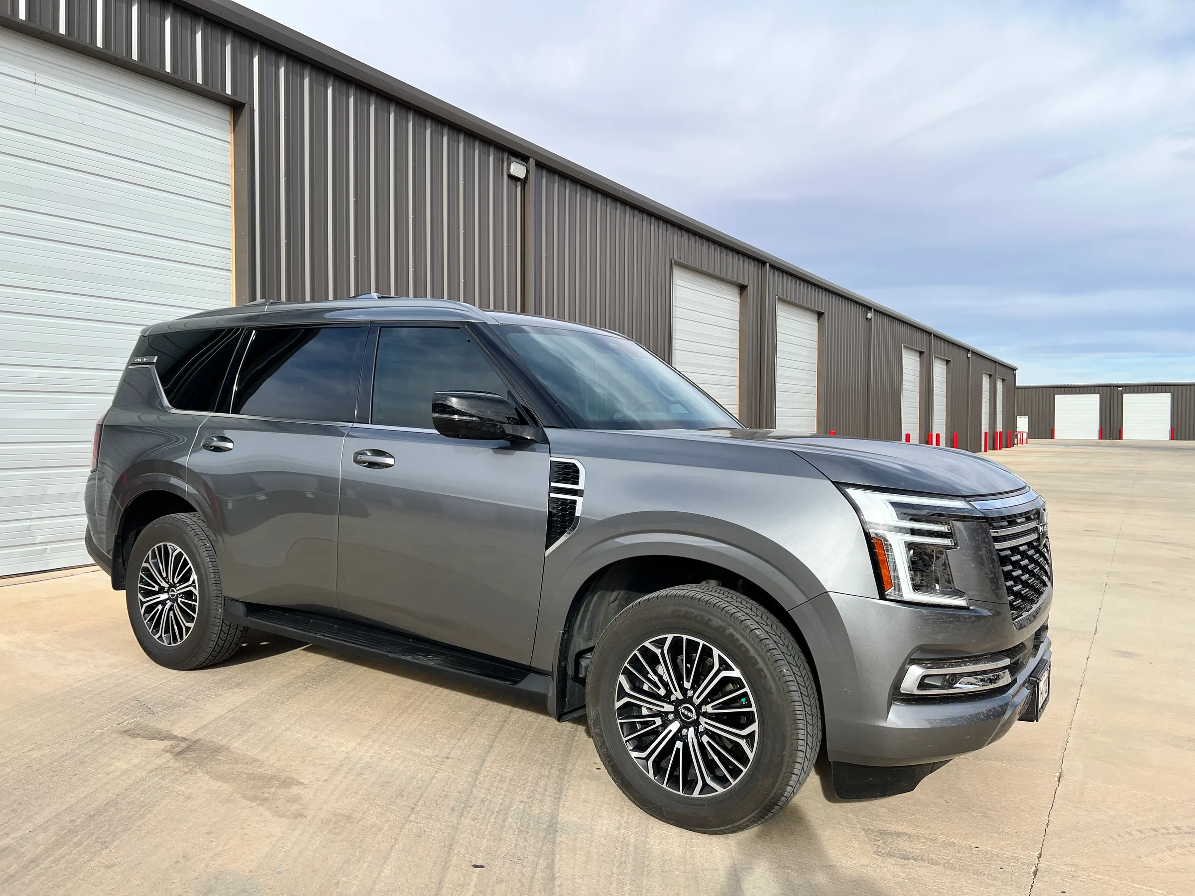 Gray Nissan Armada with dark window tint applied to all windows, displayed in front of an industrial building.