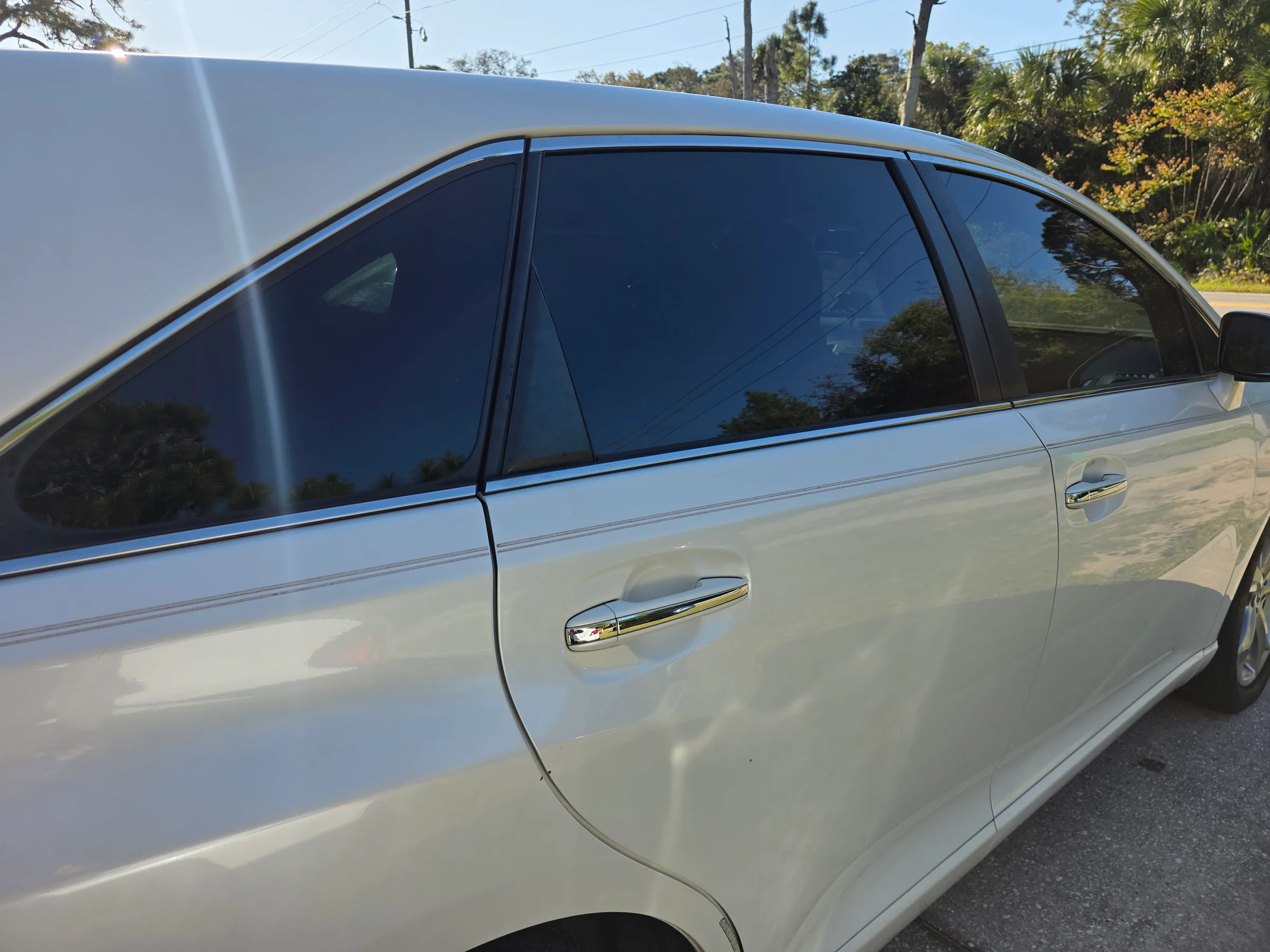 Silver SUV with dark window tint applied to the rear passenger windows, parked outdoors with trees visible in the background.