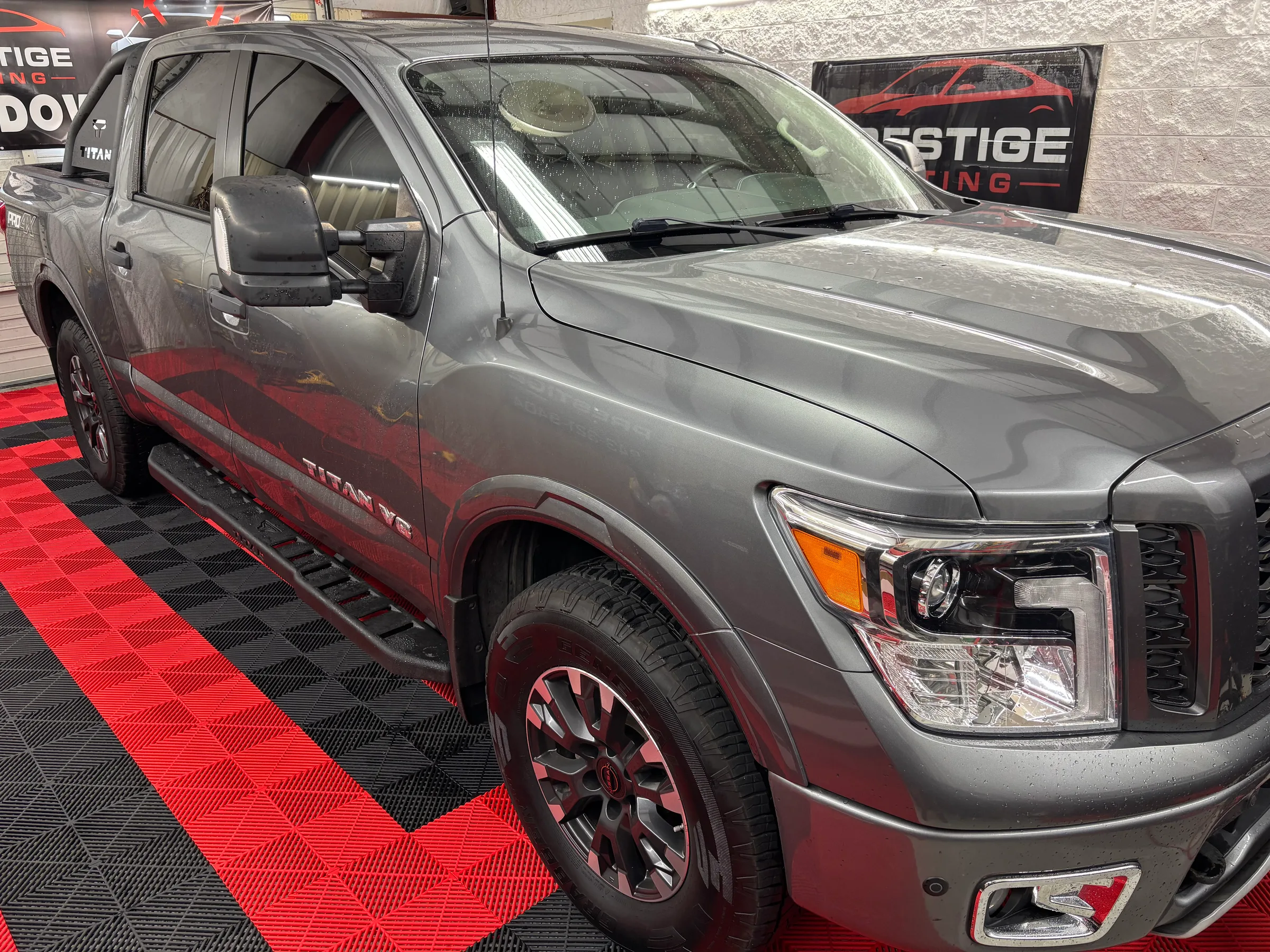 Silver and red Nissan Titan pickup truck with tinted windows displayed in a showroom with red and black checkered flooring and Prestige Tinting signage.