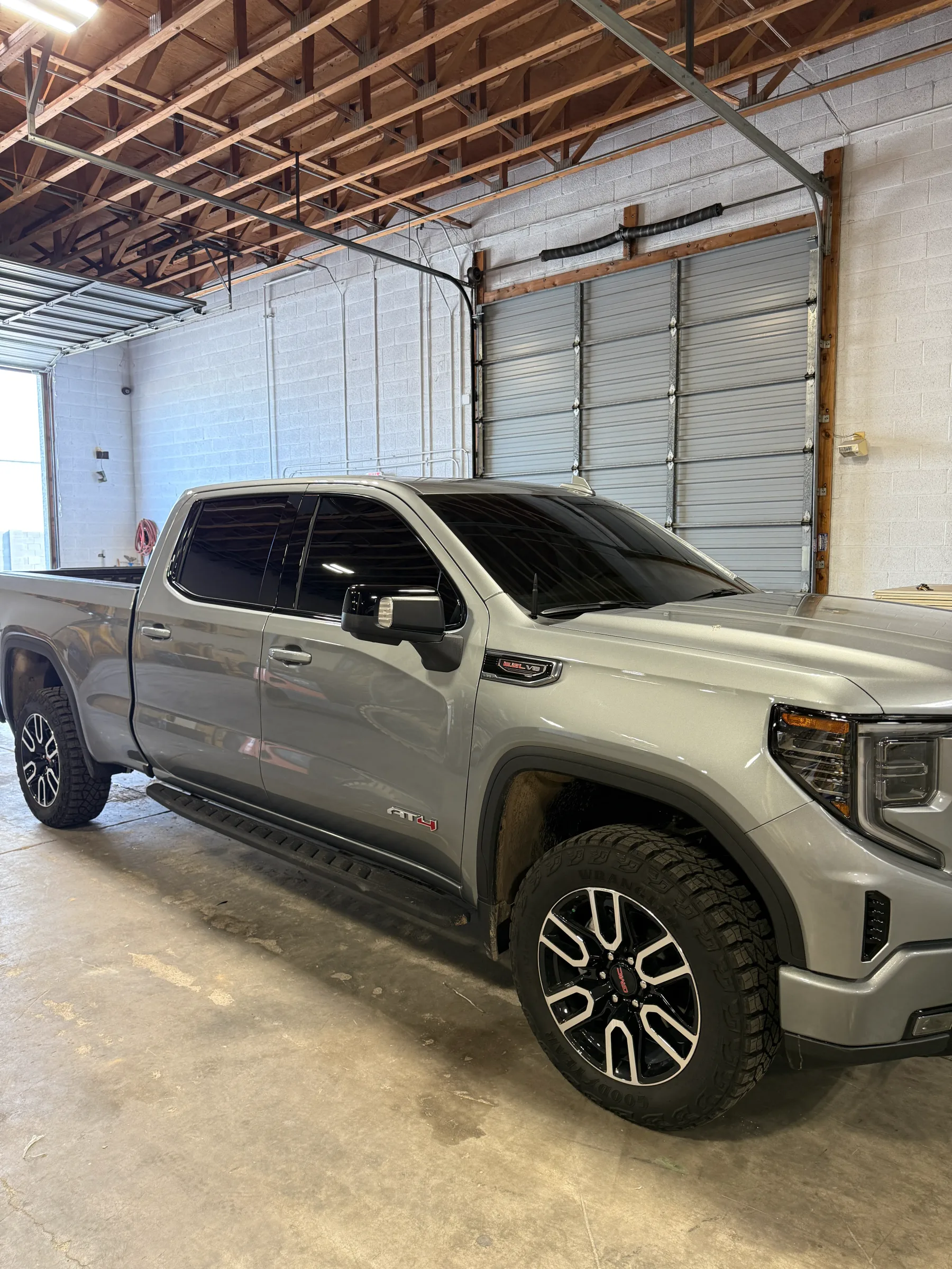 Silver GMC Sierra pickup truck with dark window tint applied, displayed in a work bay at an automotive shop.