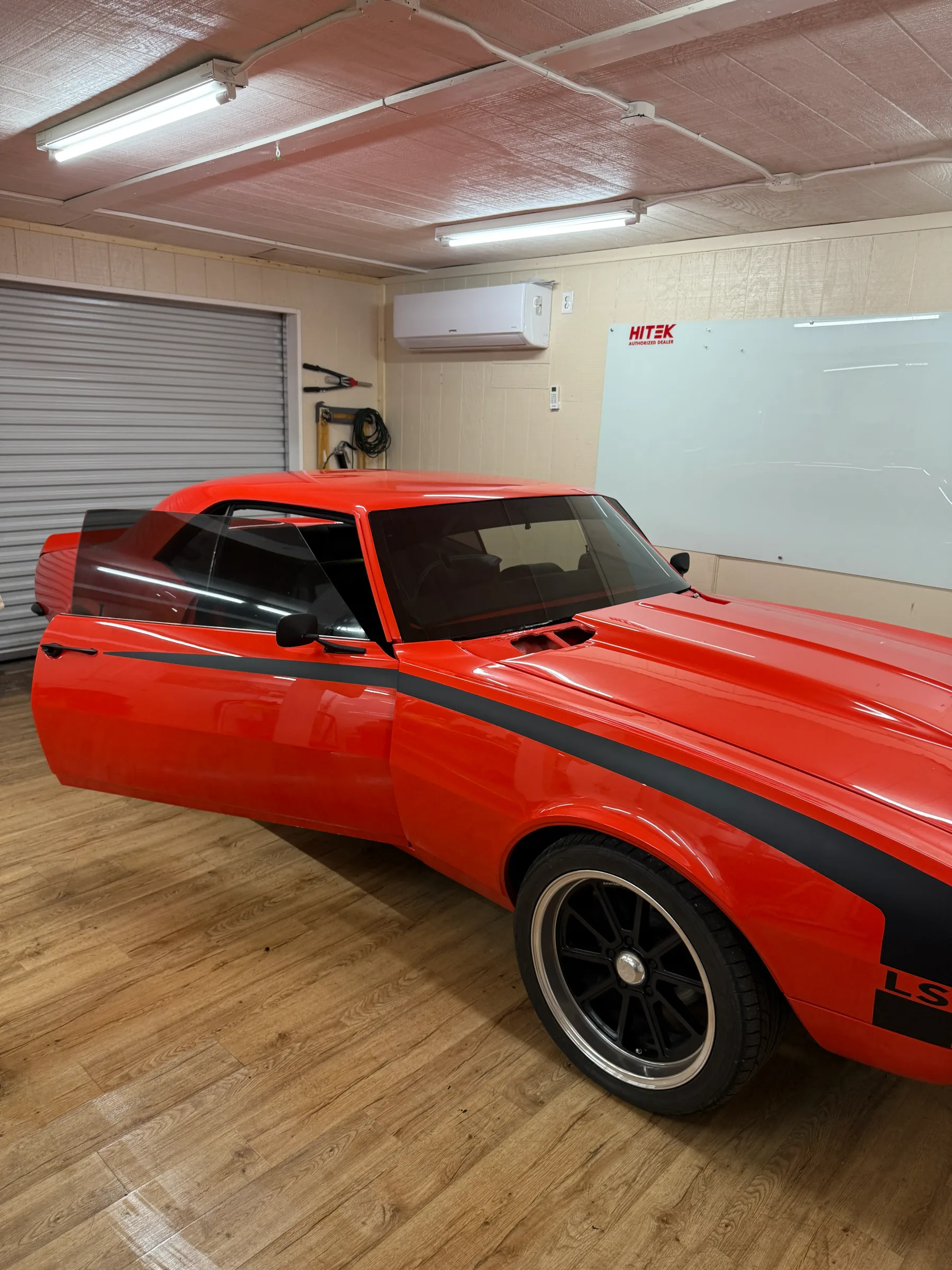 A red muscle car with darkly tinted windows parked in a detail shop garage.